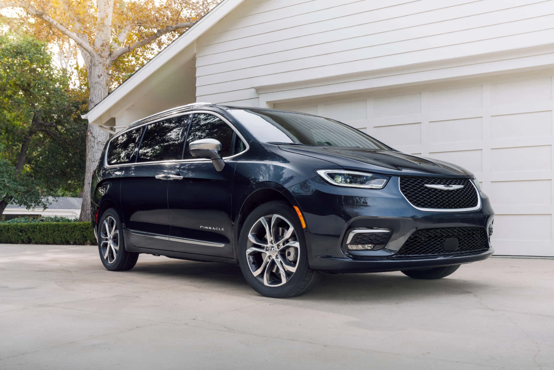 Chrysler Pacifica 桌布 壁紙 — 一架時尚的黑色Chrysler Pacifica小型貨車停在白色車庫前，背景有樹木和柔和陽光。