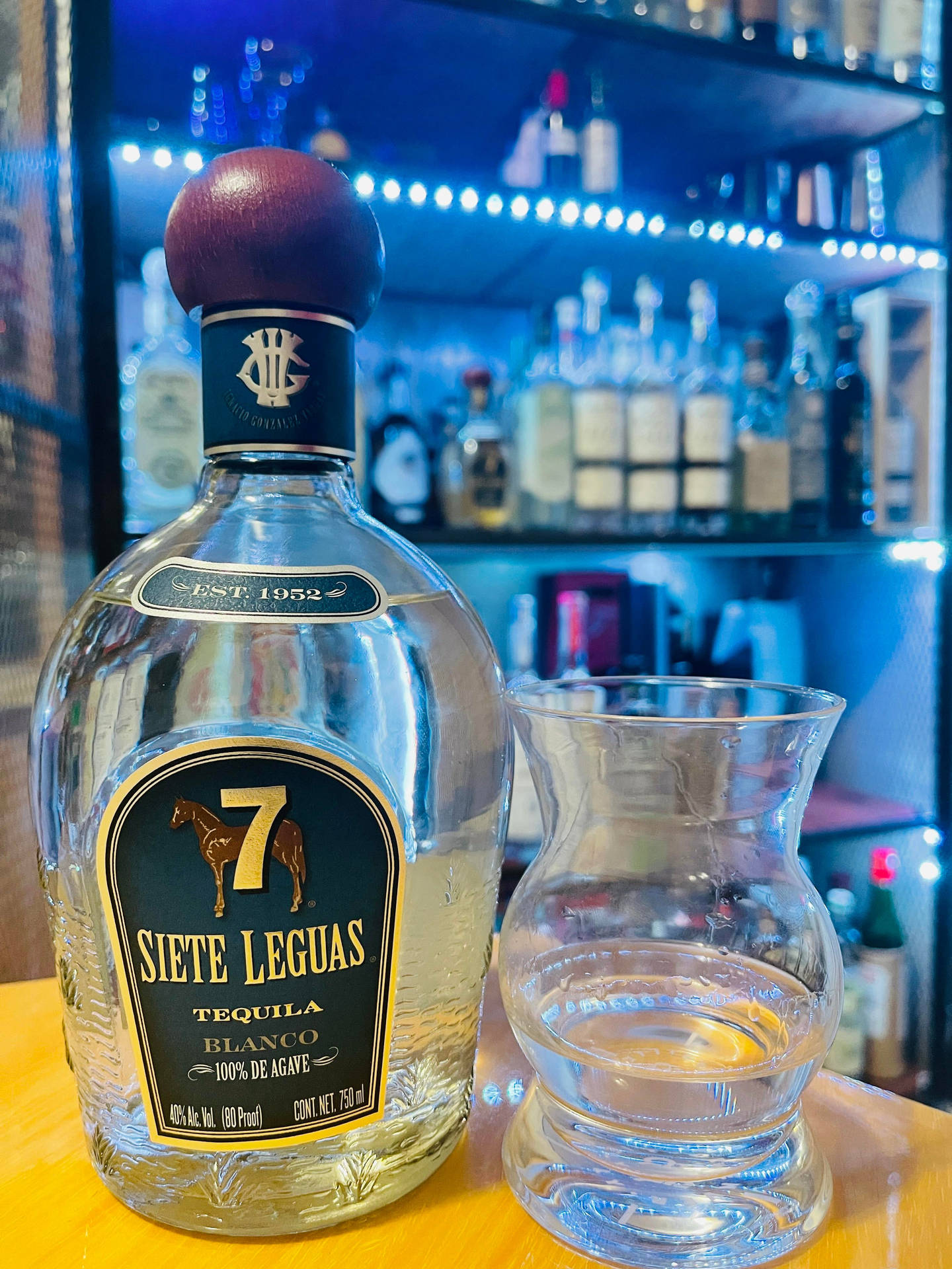 吧檯上的一瓶龍舌蘭酒和玻璃杯，背景有藍色燈光。