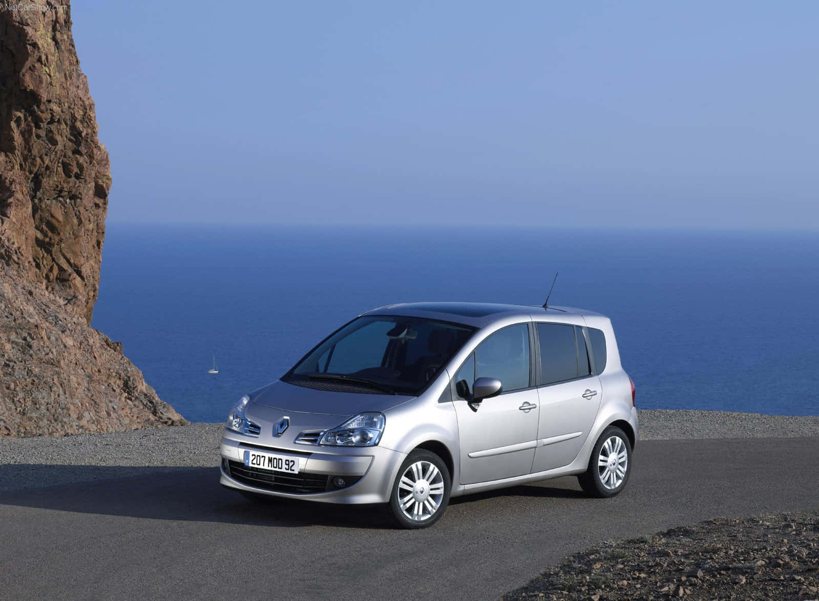 Renault Modus 桌布 壁紙 — 一輛銀色雷諾Modus停泊在海岸懸崖道路上，俯瞰著廣闊的藍色海洋，遠處有一艘帆船。