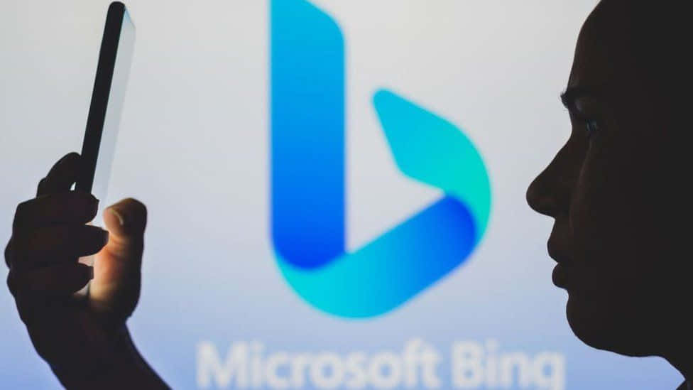 一個人手持電話站在 Microsoft Bing 標誌投影前。