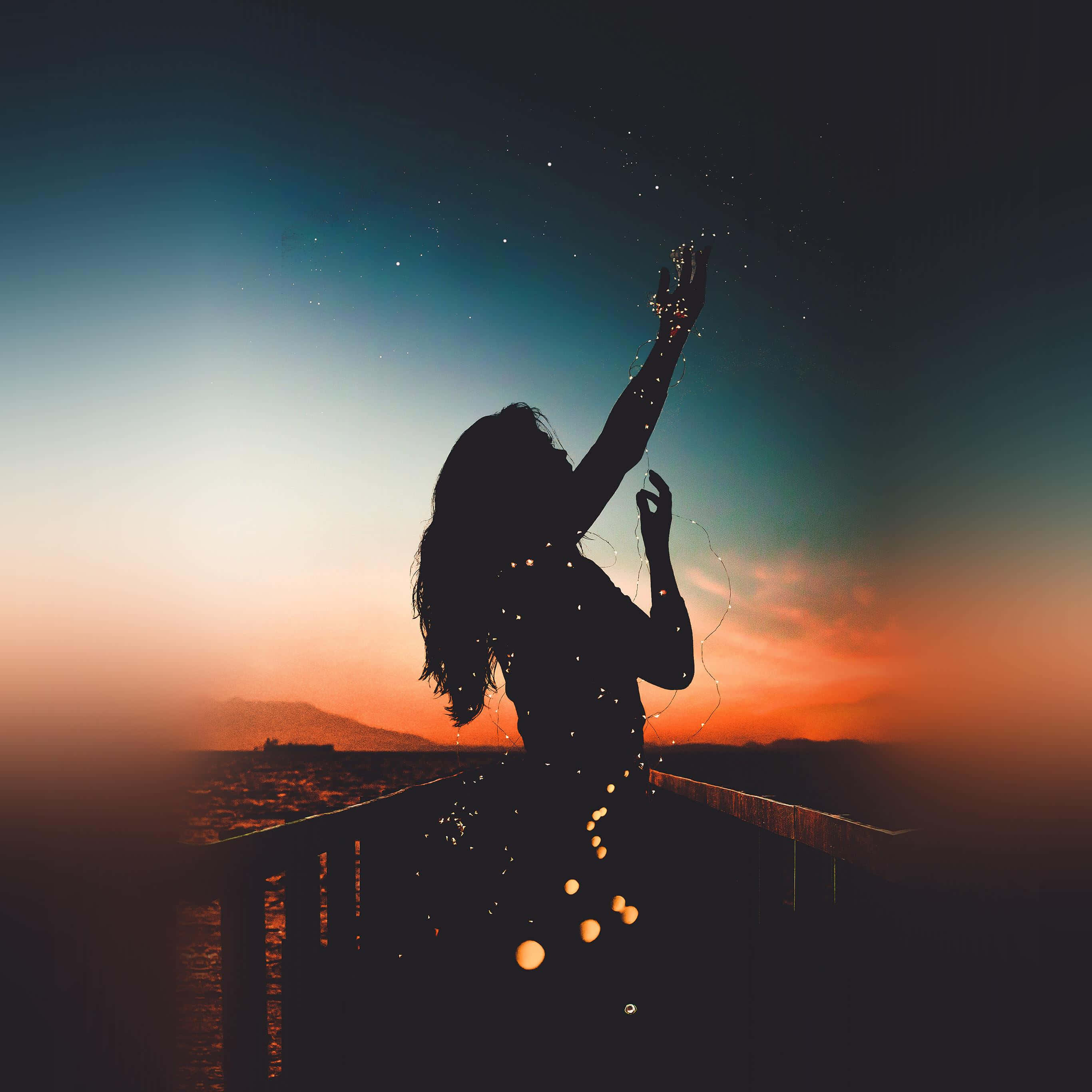 Sunset Silhouette 桌布 壁紙 — 一個人在暮色中的碼頭上伸手觸摸星星的剪影，周圍有發光的粒子旋轉環繞。