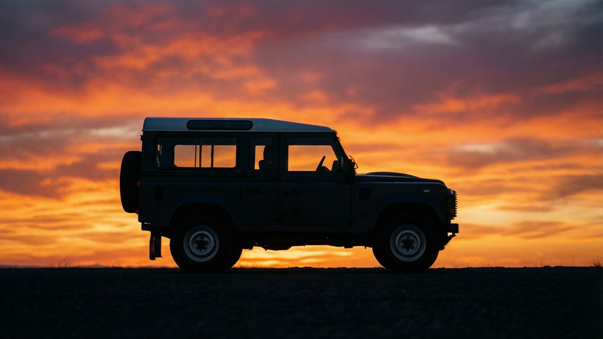 在荒蕪的景觀上，日落時分 Land Rover Defender 的剪影。