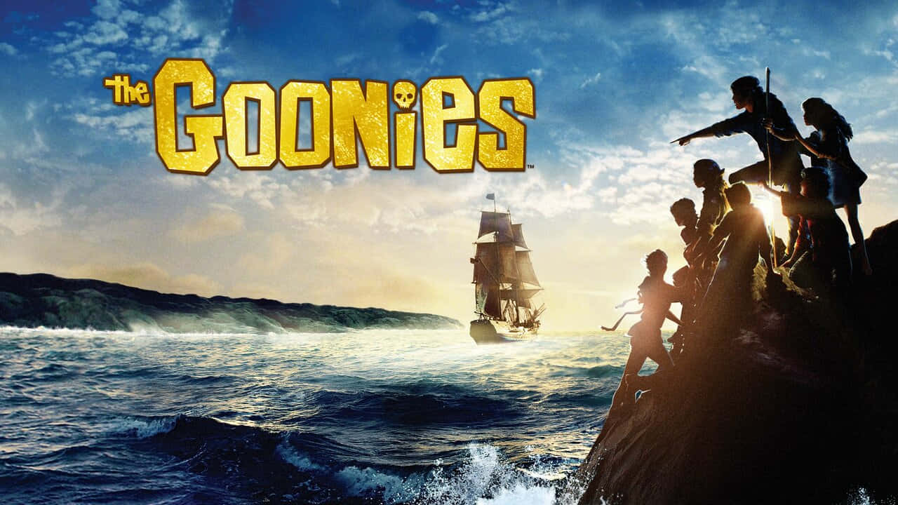  壁紙 — 剪影小孩在懸崖上凝視著金色夕陽天空下的帆船，帶有『The Goonies』標題。