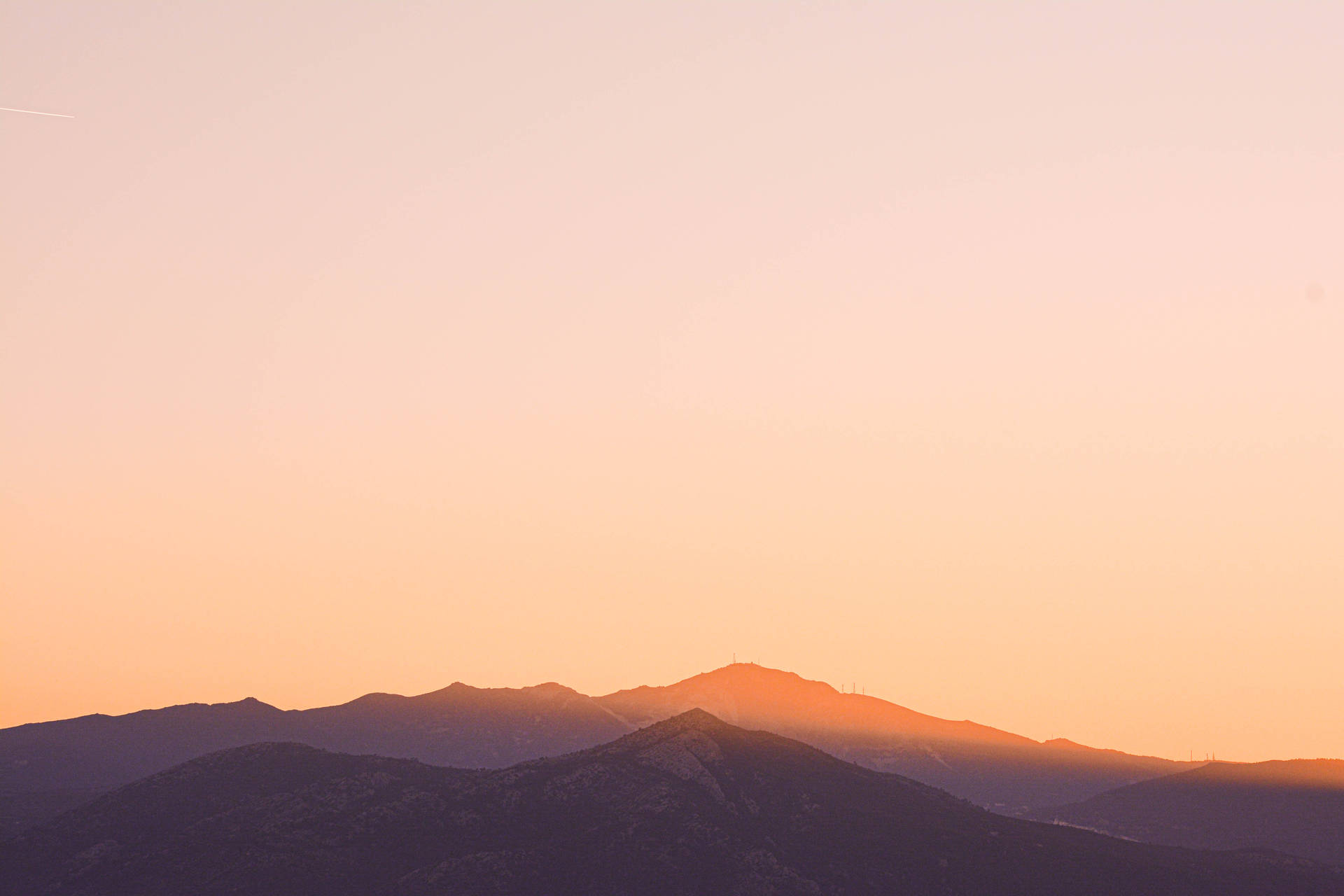 寧靜山巔剪影 壁紙 — 山脈剪影沐浴在溫暖的橙色夕陽餘暉中，映襯著柔和的漸變天空。