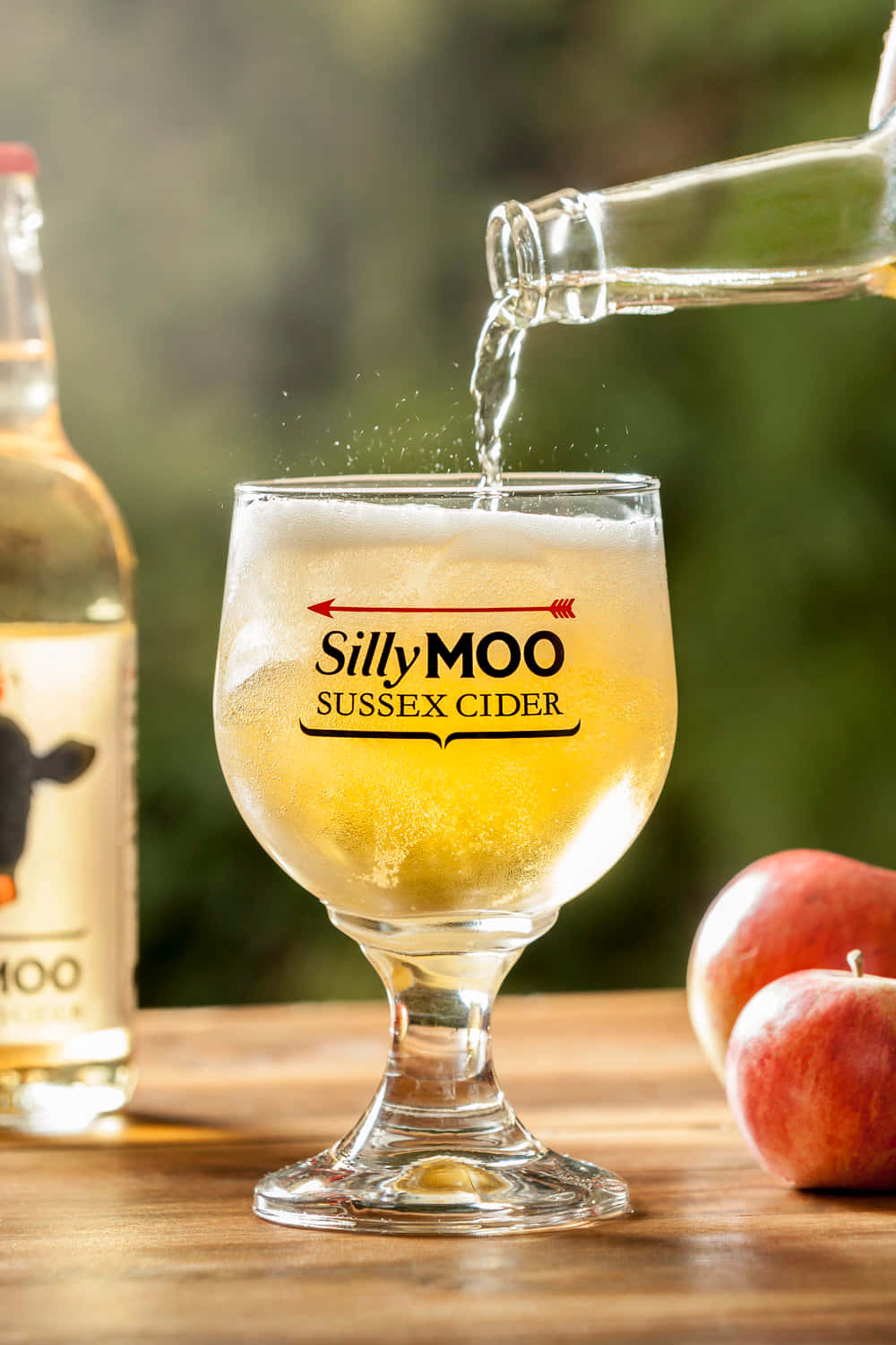 Silly Moo Sussex Cider 正在倒入一個玻璃杯，附近有蘋果。