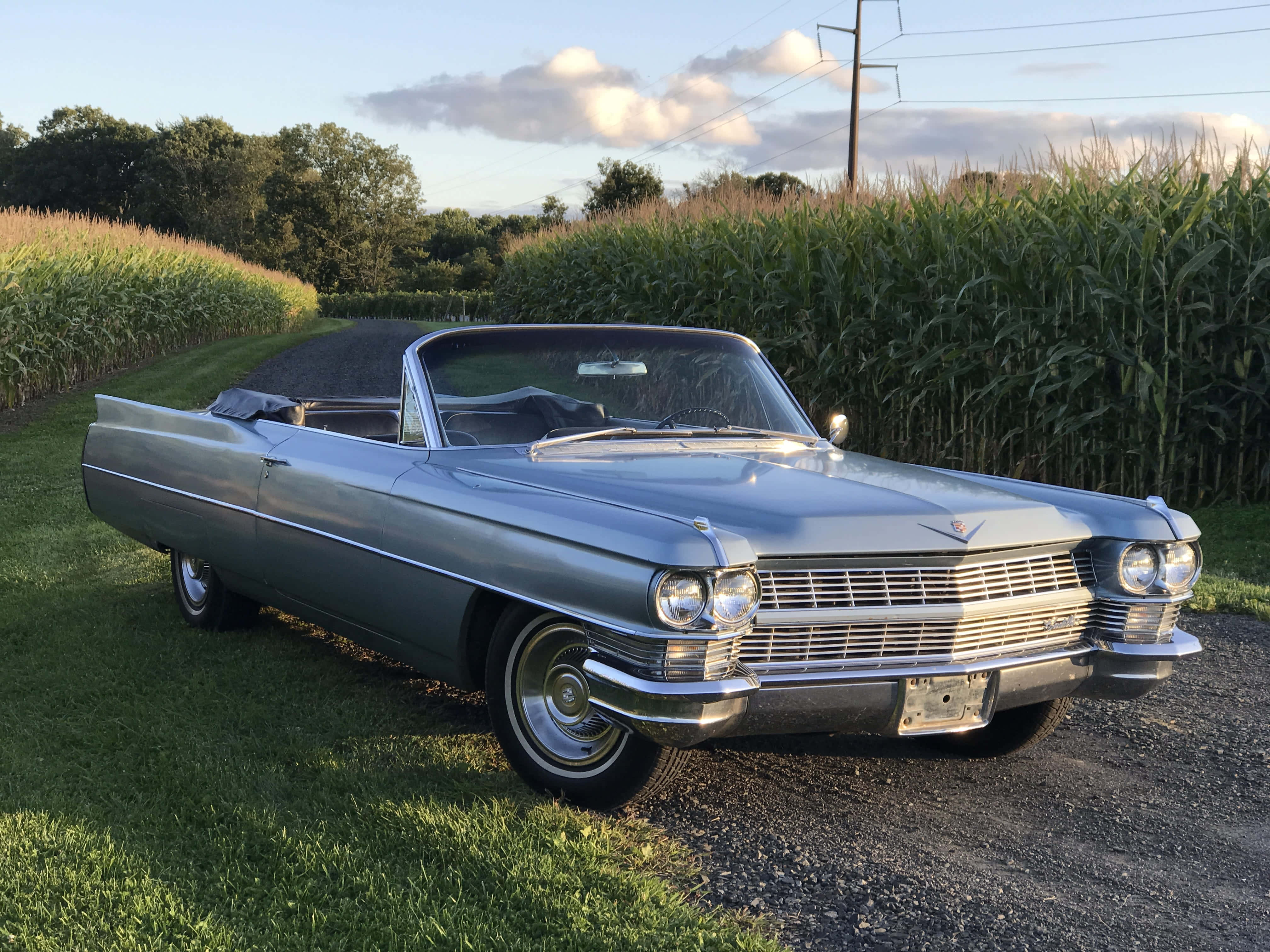 Cadillac Deville 桌布 壁紙 — 一輛銀色1960年代凱迪拉克開篷車停泊在日落時分高聳玉米田旁的碎石路上。