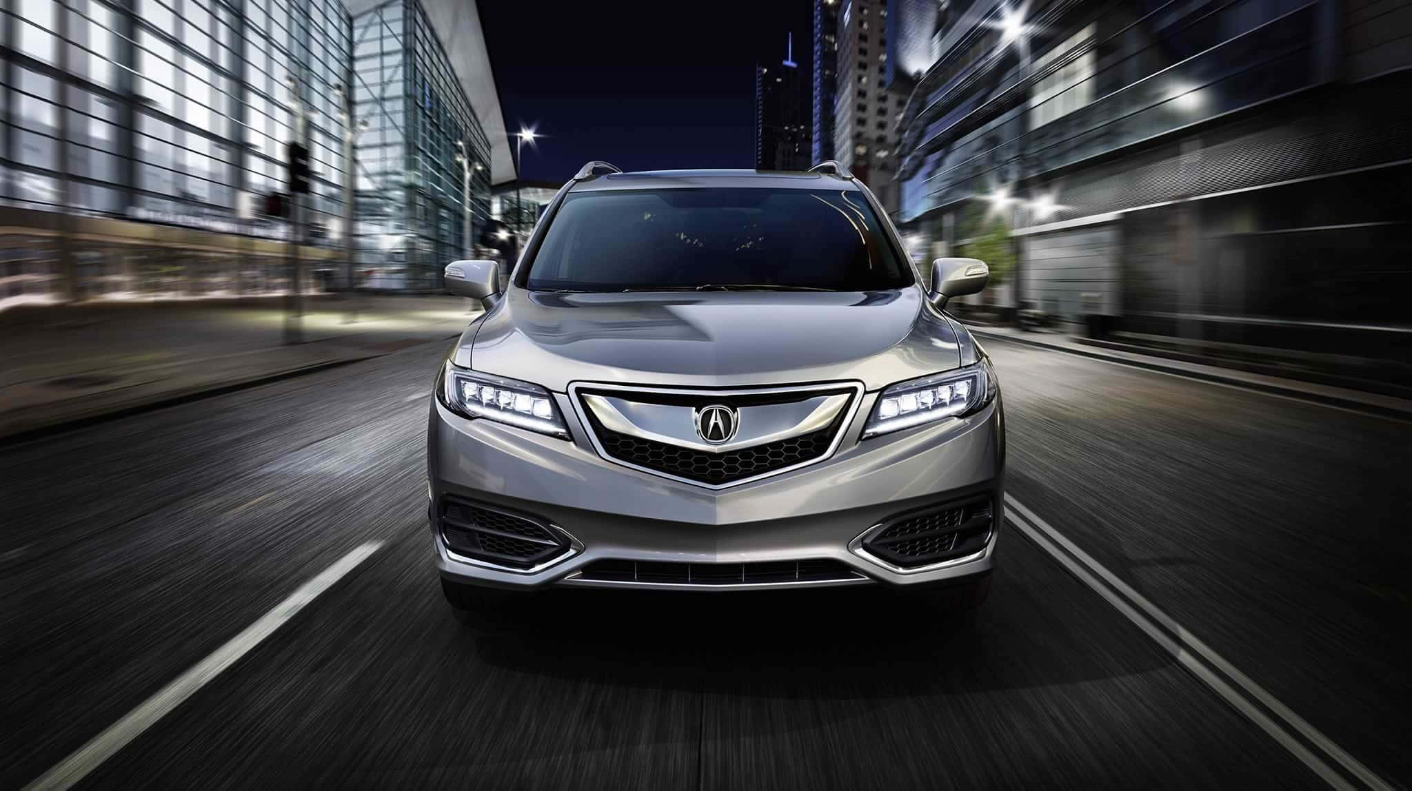 Acura Rdx 桌布 壁紙 — 一輛銀色Acura SUV在夜晚霓虹燈閃爍的城市街道上飛馳，背景是模糊的摩天大樓。