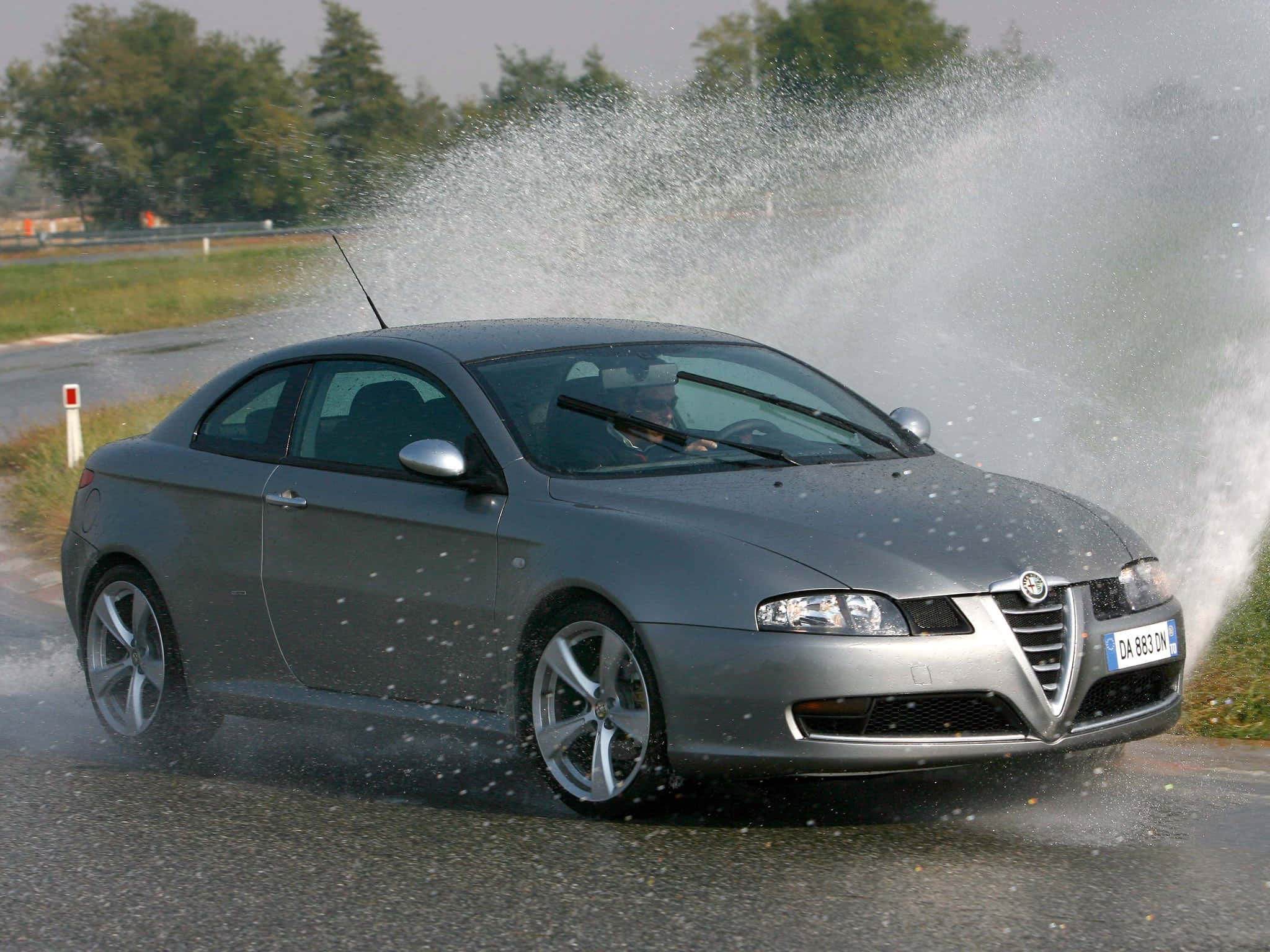 Alfa Romeo Gt 桌布 壁紙 — 一輛銀色愛快羅密歐跑車在潮濕彎道高速行駛，在路邊賽道上戲劇性地濺起水花。