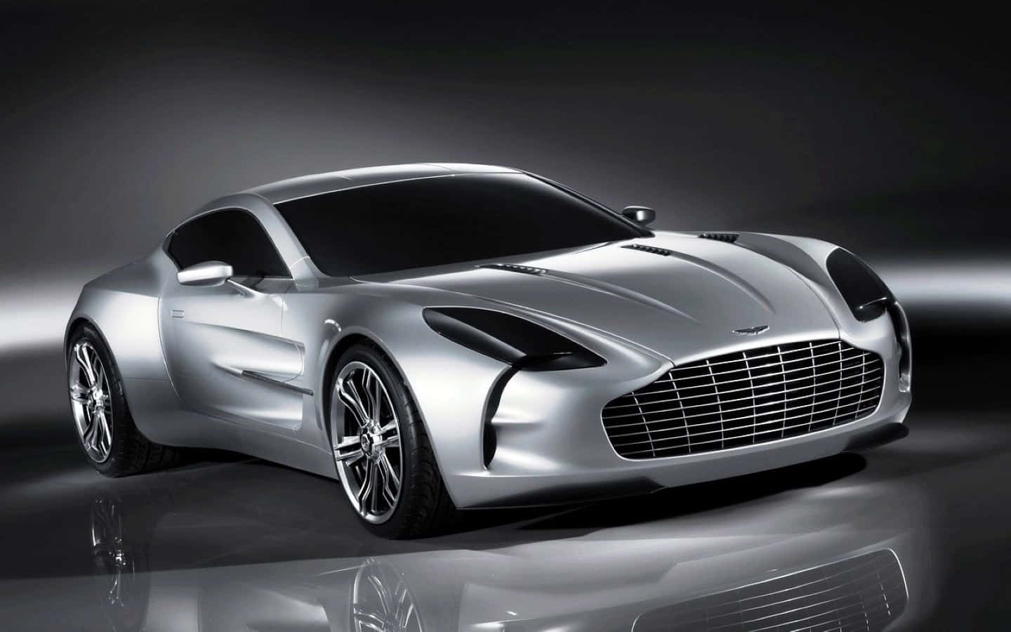Aston Martin One-77 桌布 壁紙 — 一輛時尚的銀色 Aston Martin 跑車在攝影棚燈光下，於反光的黑色表面上閃閃發光。