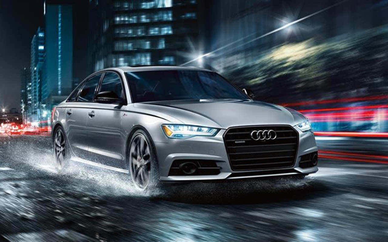 Audi S6 桌布 壁紙 — 一輛銀色 Audi 房車在夜間飛馳於雨濕的街道上，模糊的霓虹燈光掠過。