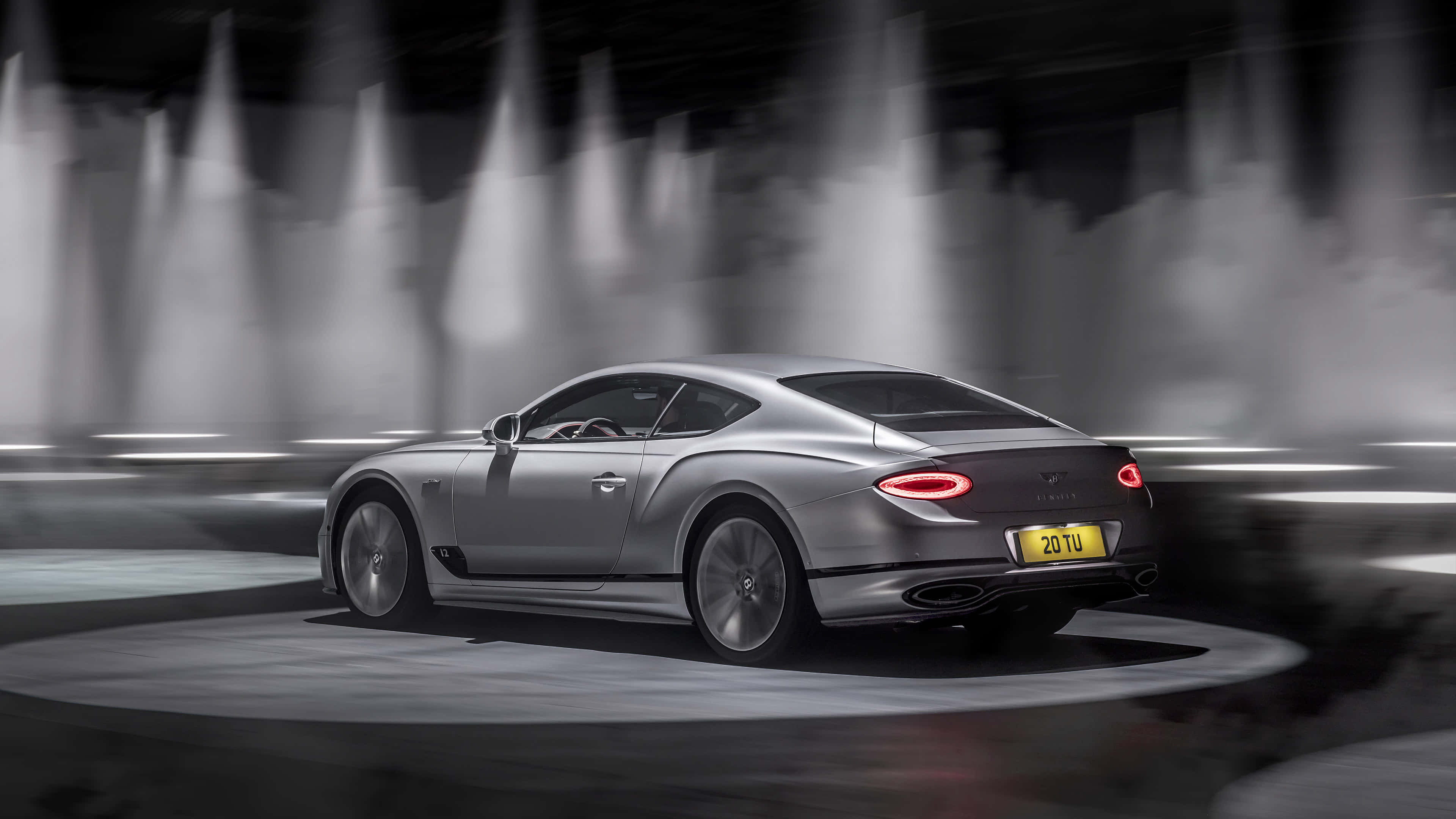 Bentley Continental Gt 桌布 壁紙 — 一輛時尚的銀色賓利 Continental GT 在煙霧瀰漫的隧道中疾馳，隧道被戲劇性的聚光燈照亮。
