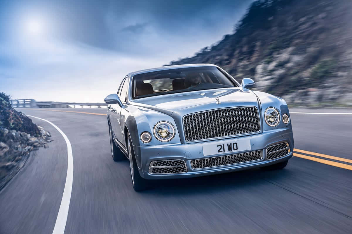 Bentley Mulsanne 桌布 壁紙 — 一輛銀色賓利Mulsanne在明亮的藍天下，沿著蜿蜒的山路疾馳，帶有動態模糊效果。