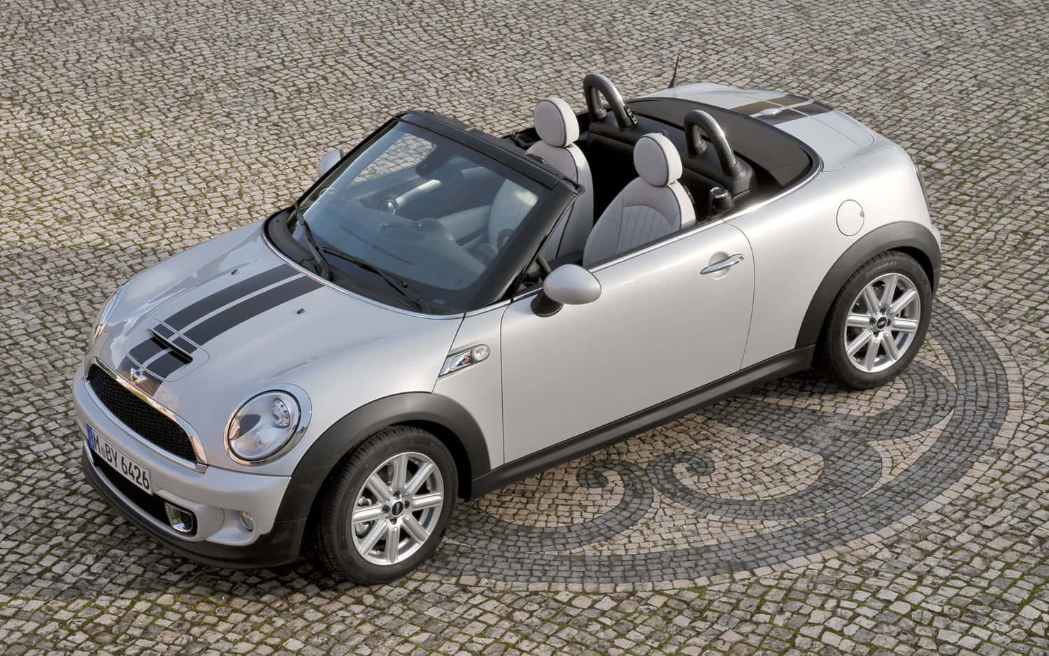  壁紙 — 一輛銀色開篷Mini Cooper，帶有黑色賽車條紋，停在有圖案的鵝卵石廣場上。