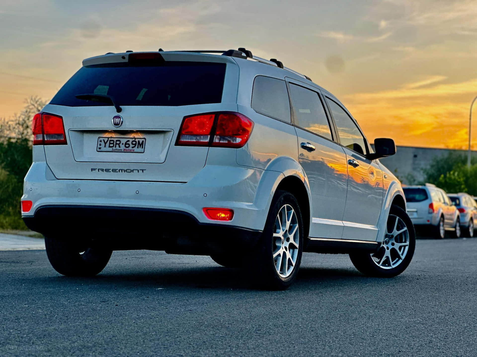  壁紙 — 一輛銀色 Fiat Freemont SUV 在日落時停泊，溫暖的金色光線反射在其後部和側面板上。