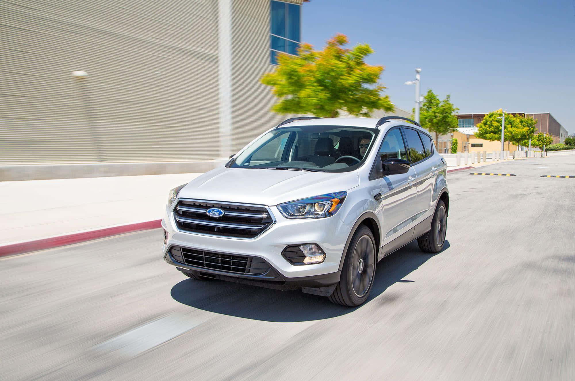 Ford Escape 桌布 壁紙 — 一輛銀色福特Escape SUV在陽光明媚的城市街道上飛馳，路面和背景樹木呈現動態模糊效果。