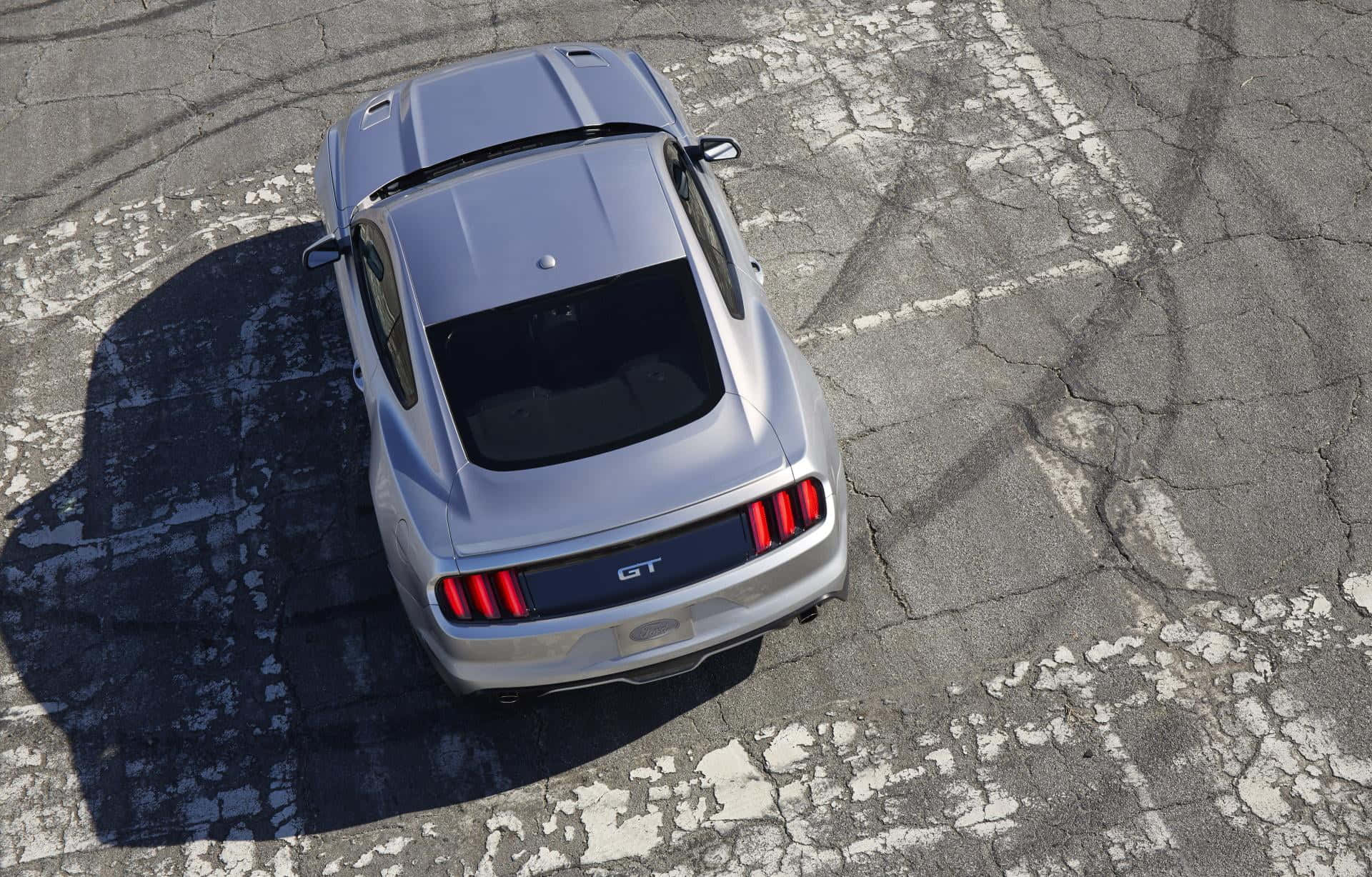 Ford Mustang California Special 桌布 壁紙 — 一輛銀色福特Mustang GT停泊在裂開的瀝青路上，帶有鮮明的輪胎痕跡和尖銳的陰影，在明亮的陽光下。