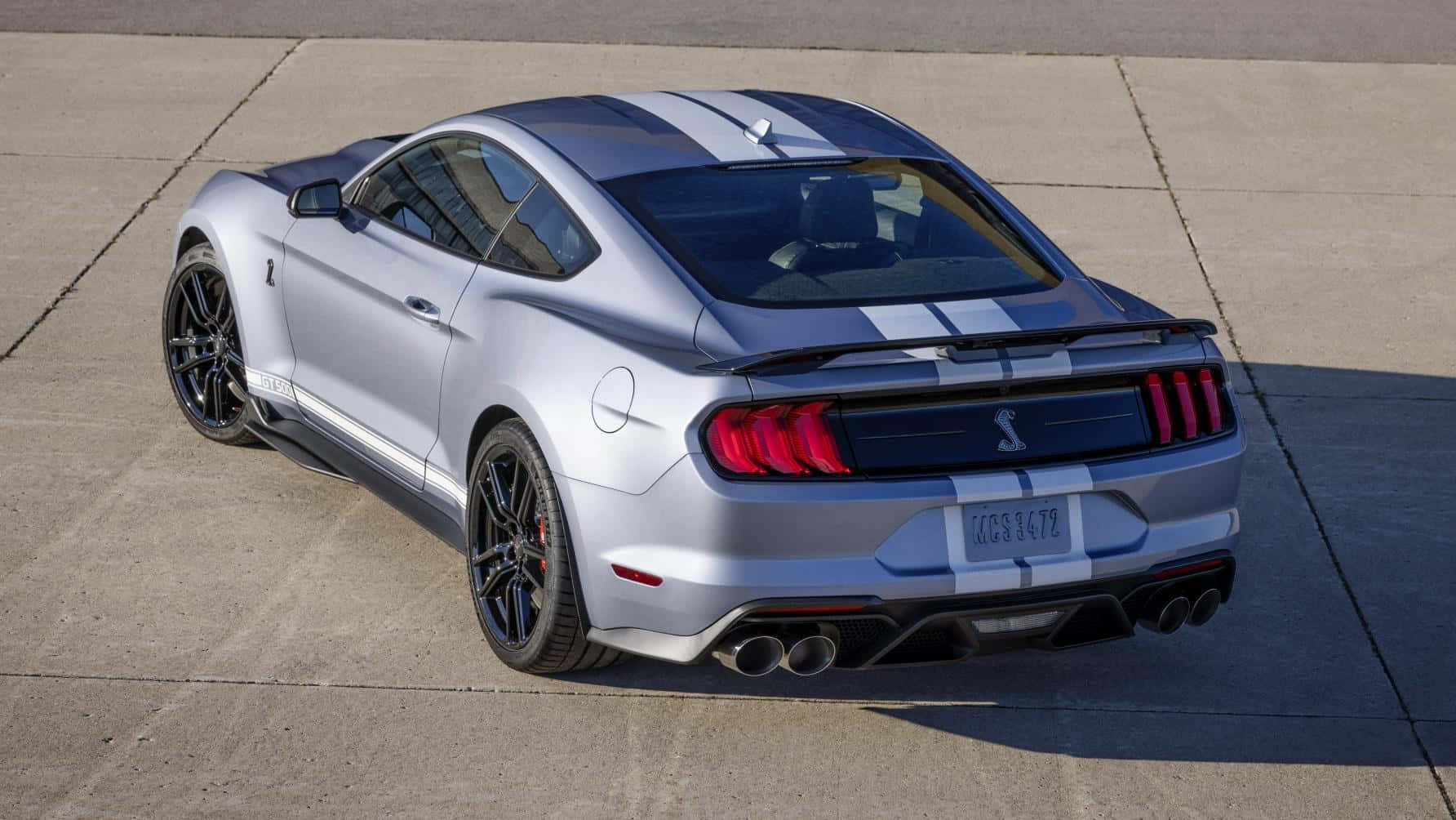  壁紙 — 一輛銀色福特Mustang Shelby GT350R，帶有黑色條紋和紅色尾燈，停在陽光明媚的混凝土場地上。