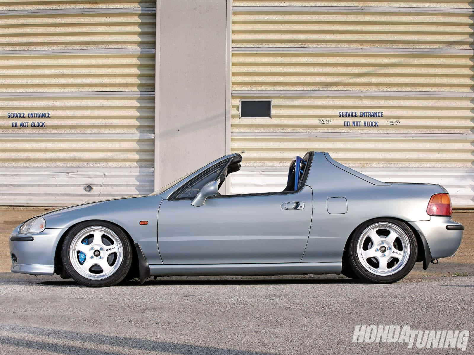 Honda Civic Del Sol 桌布 壁紙 — 一輛銀色本田S2000開篷跑車停泊在米色波紋金屬車庫門前，門上有服務入口標誌。