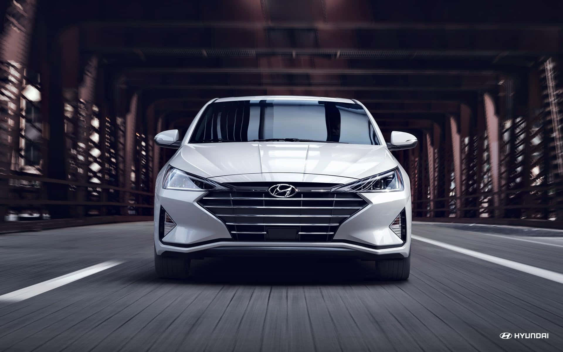 Hyundai Elantra 桌布 壁紙 — 一輛時尚的銀色現代汽車在橋上行駛，背景有動態模糊和工業鋼樑。