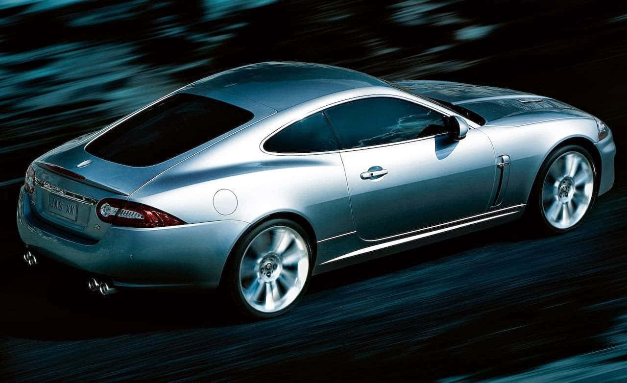 Jaguar Xkr 桌布 壁紙 — 一架流線型銀色積架XK轎跑車在模糊的夜間場景中疾馳，運動線條強調速度。