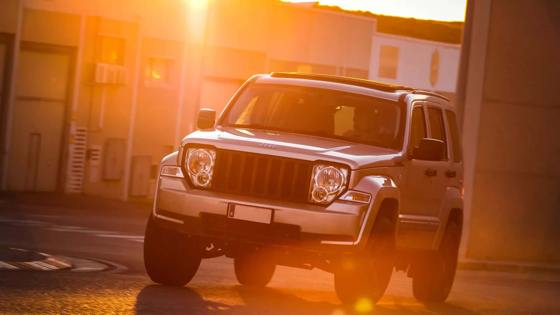 Jeep Liberty 桌布 壁紙 — 一輛銀色Jeep Wrangler停泊在都市地塊，沐浴在帶有鏡頭光暈的金色夕陽光中。