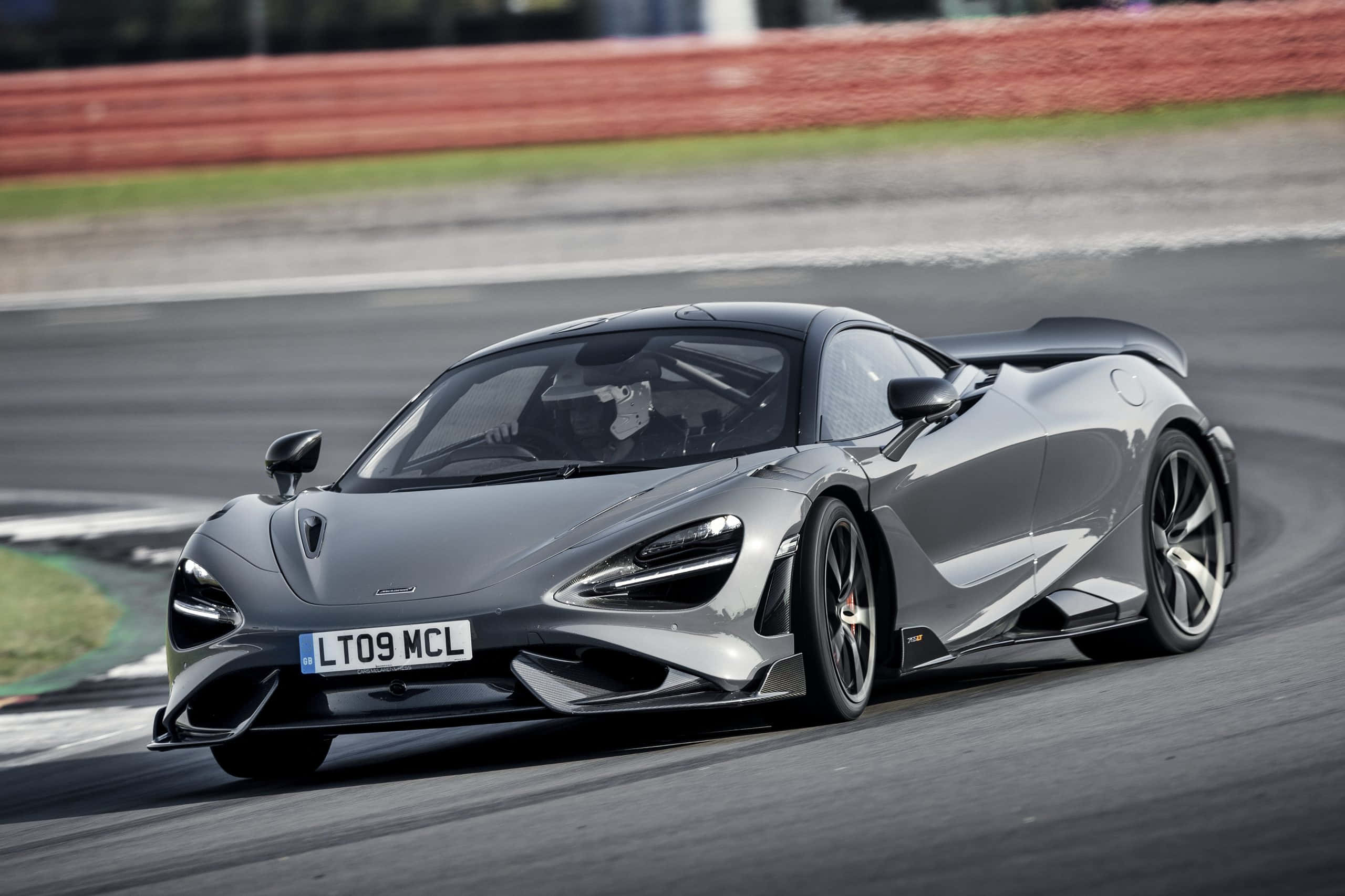 Mclaren 765lt 桌布 壁紙 — 一架流線型銀色McLaren 720S在賽道上疾馳，背景有動態模糊和紅色護欄。