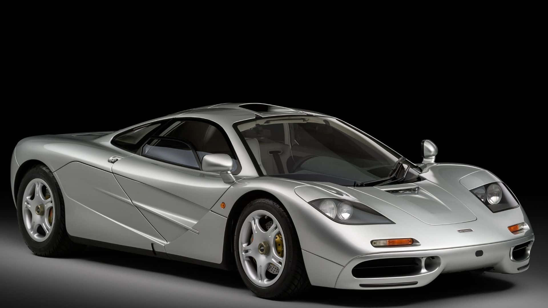 Mclaren F1 桌布 壁紙 — 一輛流線型的銀色McLaren F1超級跑車在攝影棚燈光下，於純黑背景中閃耀光芒。