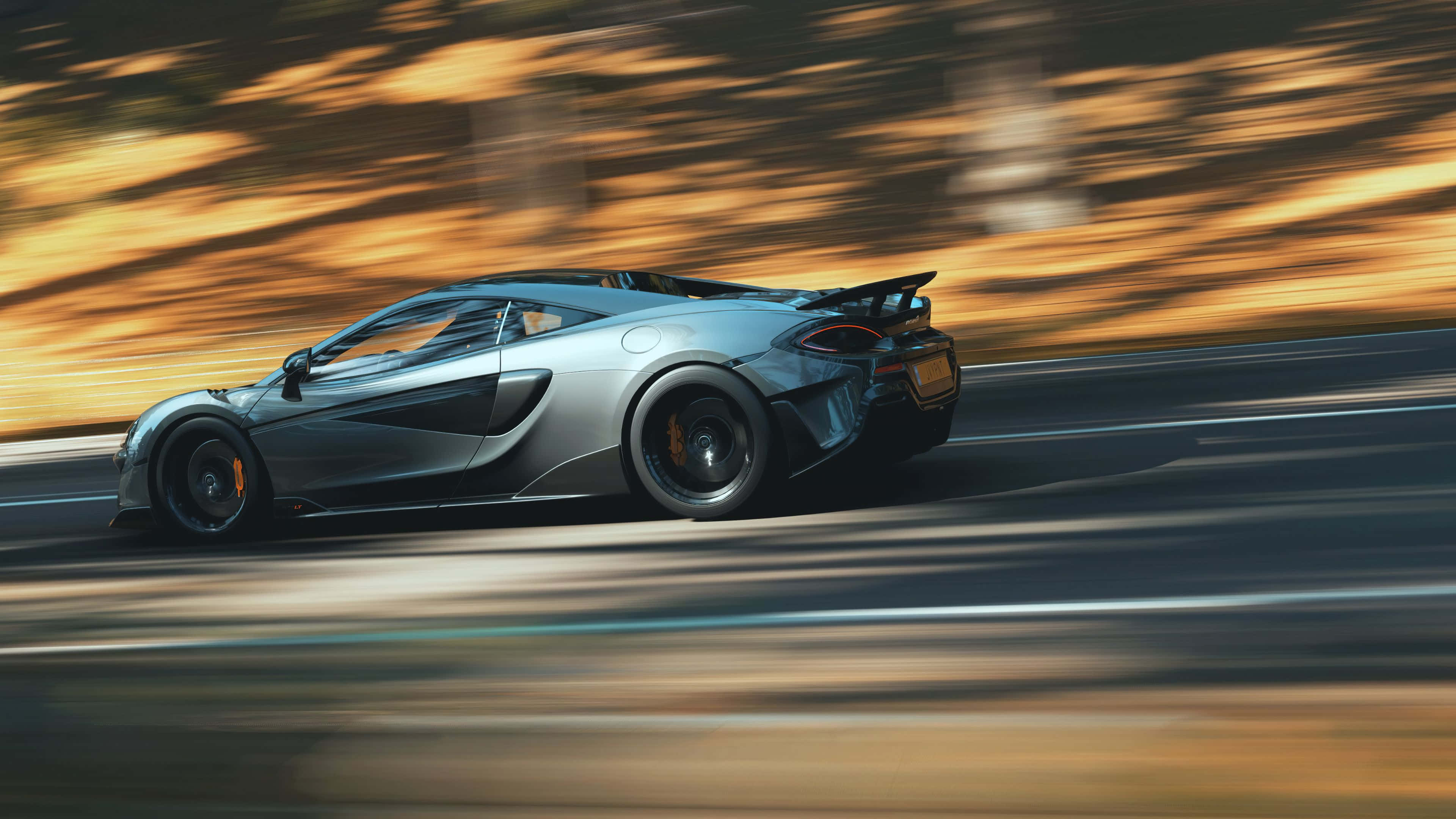 Mclaren 600lt 桌布 壁紙 — 一輛銀色McLaren跑車在道路上疾馳，背景是金色的模糊樹葉。