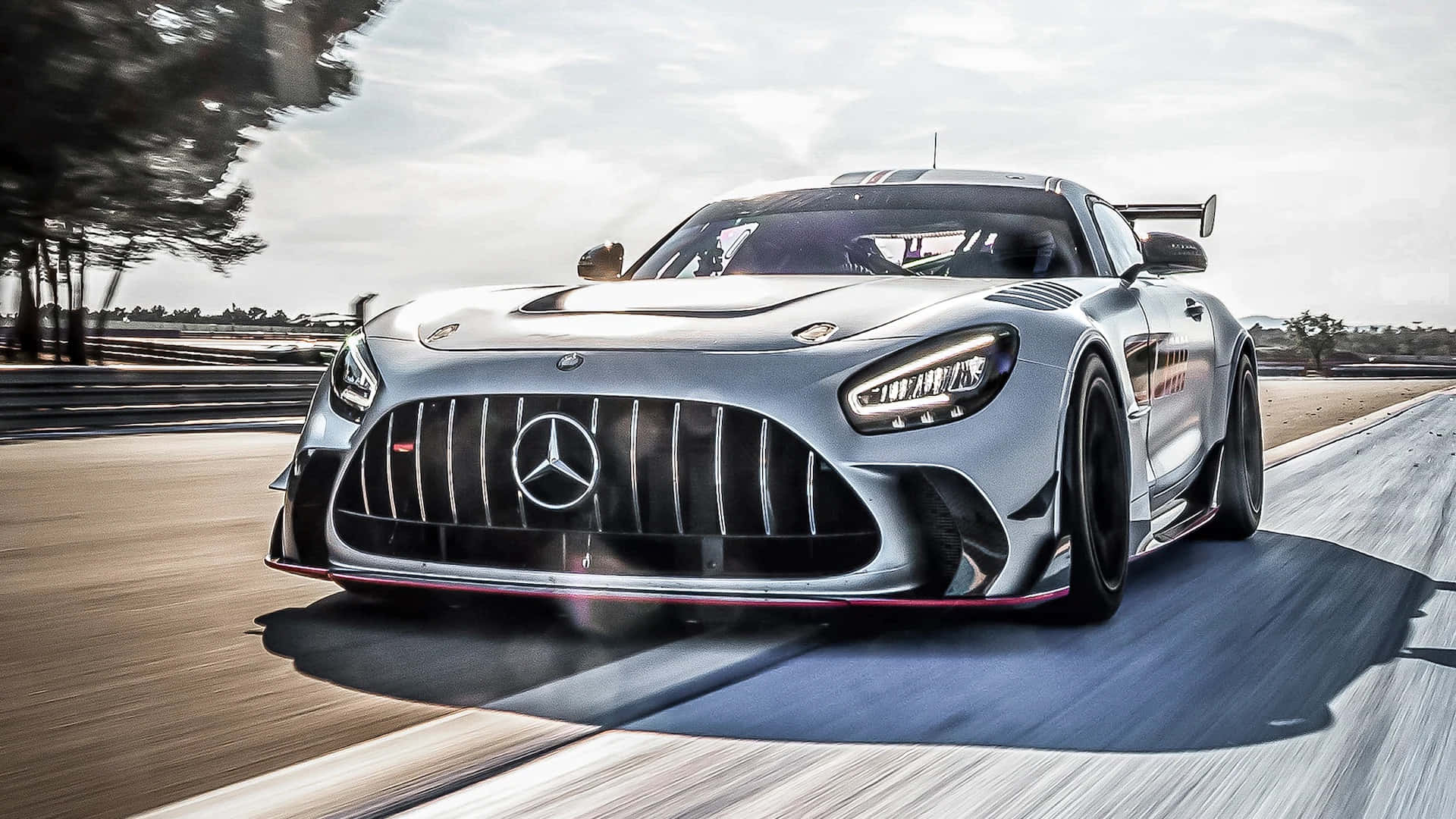 Mercedes Benz Amg Gt 桌布 壁紙 — 一輛銀色 Mercedes-AMG GT 賽車在賽道上飛馳，背景是模糊的樹木和瀝青路面。