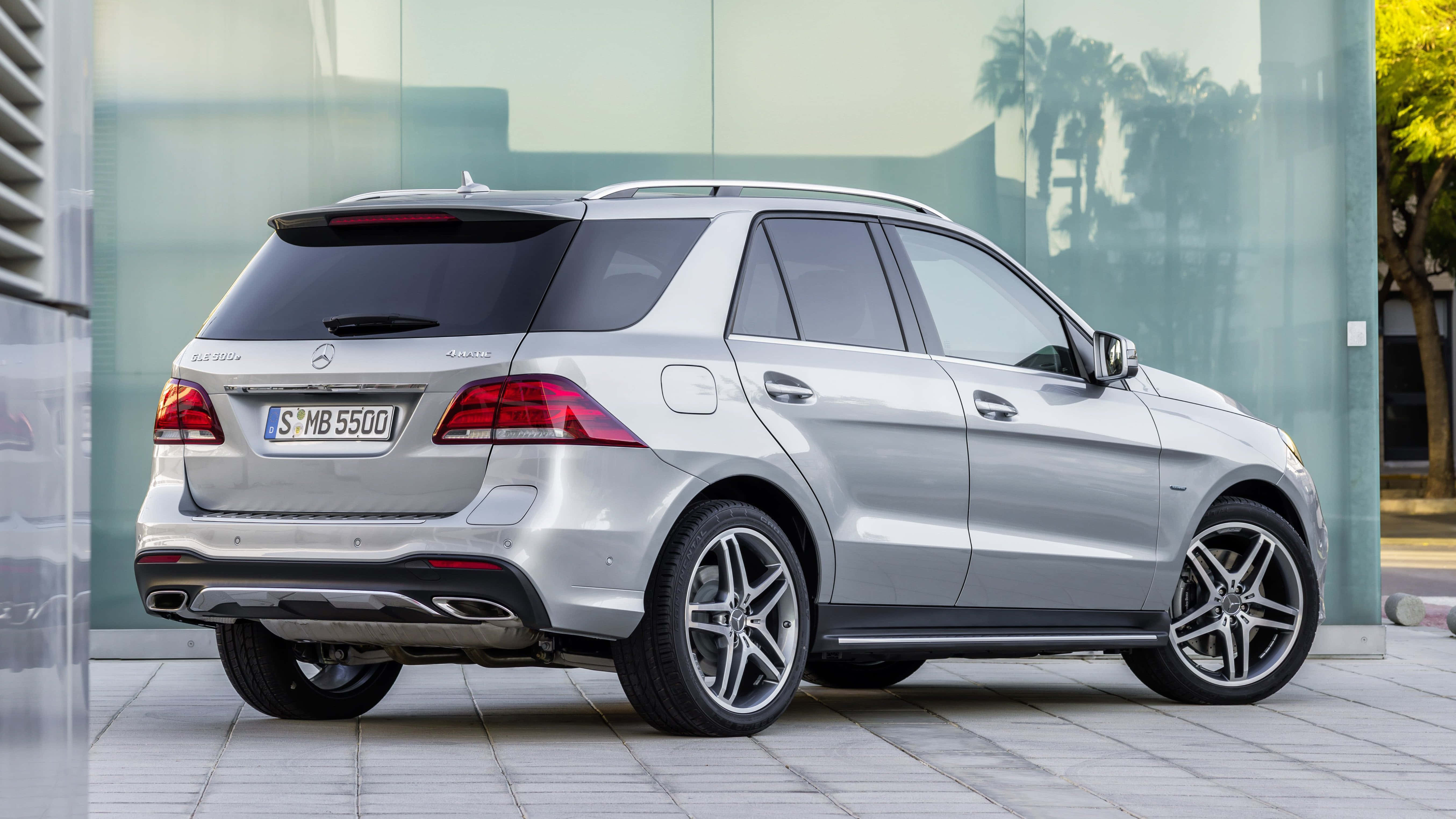 Mercedes Benz Gle-class 桌布 壁紙 — 一架時尚的銀色 Mercedes-Benz GLE SUV 停泊在瓷磚鋪砌的行人路上，旁邊是一座玻璃建築，窗戶反射出棕櫚樹。