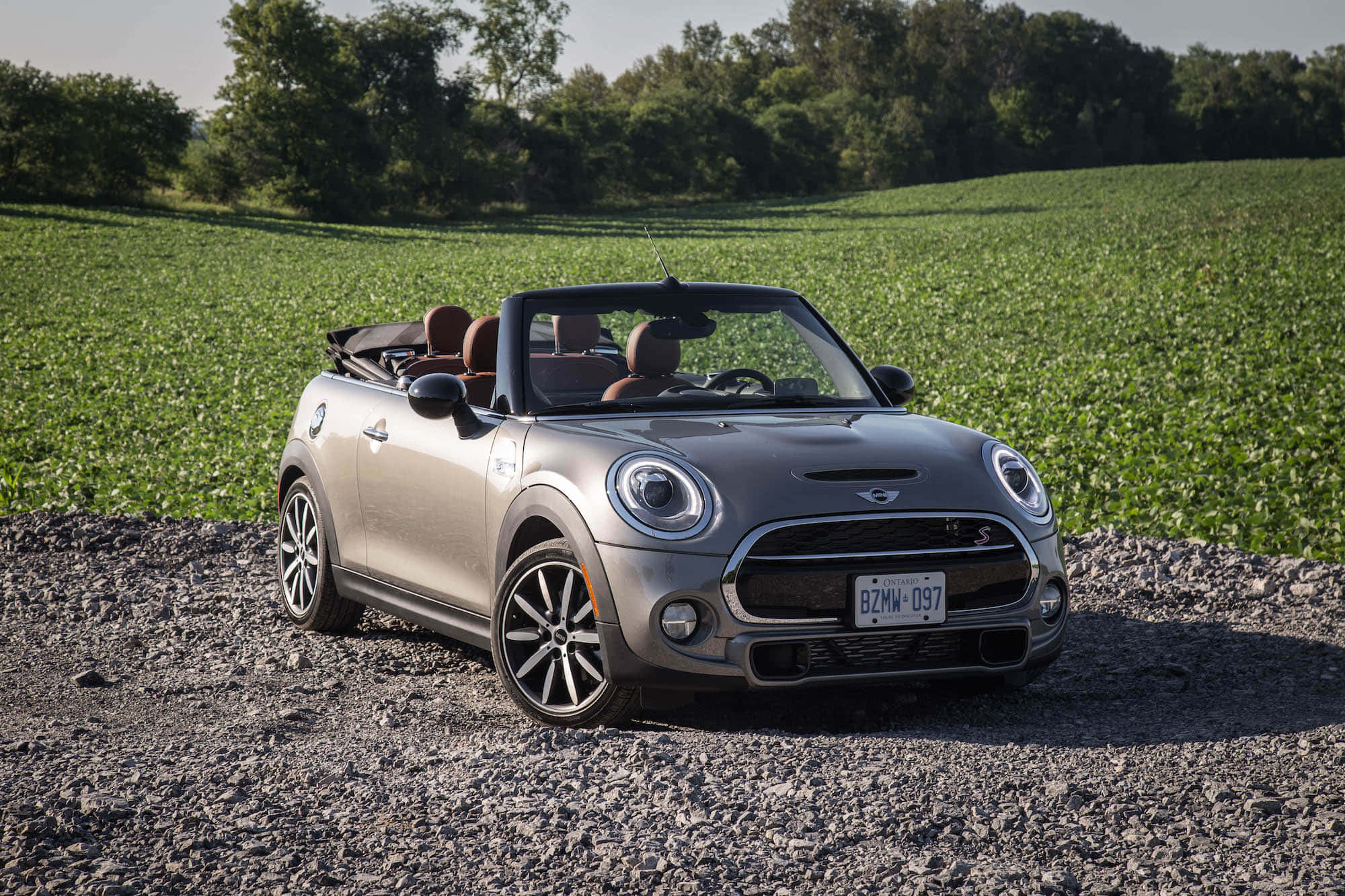 Mini Cooper S Convertible 桌布 壁紙 — 一輛銀色MINI開篷車停泊在碎石上，背景是茂密的綠色田野和樹木，在明亮的日光下。
