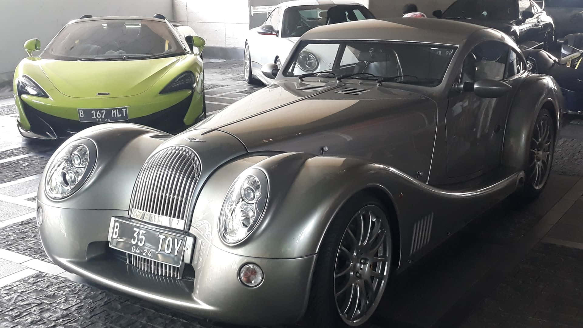 Morgan Aeromax 桌布 壁紙 — 一架時尚銀色復古風格摩根跑車醒目地停放在車庫中，旁邊是一輛充滿活力的青檸綠色麥拿侖。