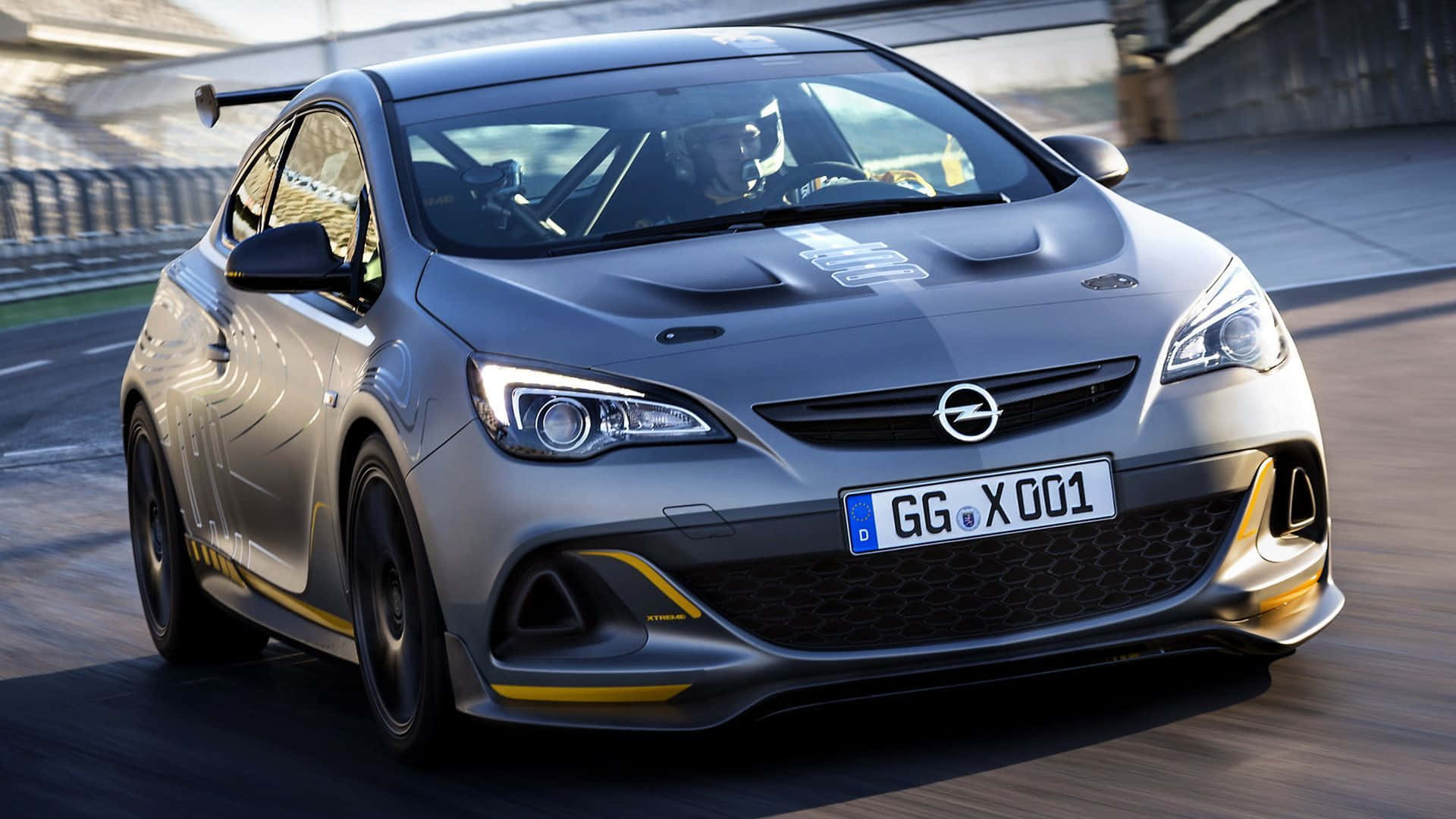 Opel Astra 桌布 壁紙 — 一輛銀色歐寶雅特GTC賽車在賽道上飛馳，帶有黃色點綴，車內司機清晰可見。