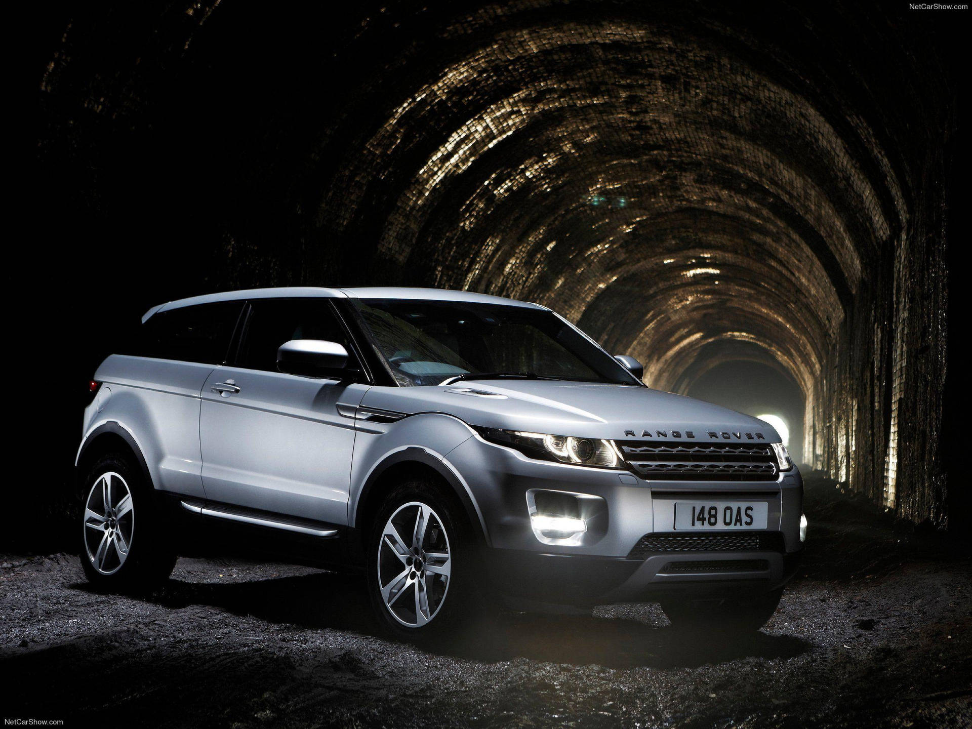 4K 路虎Range Rover隧道壁紙 壁紙 — 一輛銀色 Range Rover Evoque 在黑暗、有紋理的石隧道中，在自己的車頭燈下閃閃發光。
