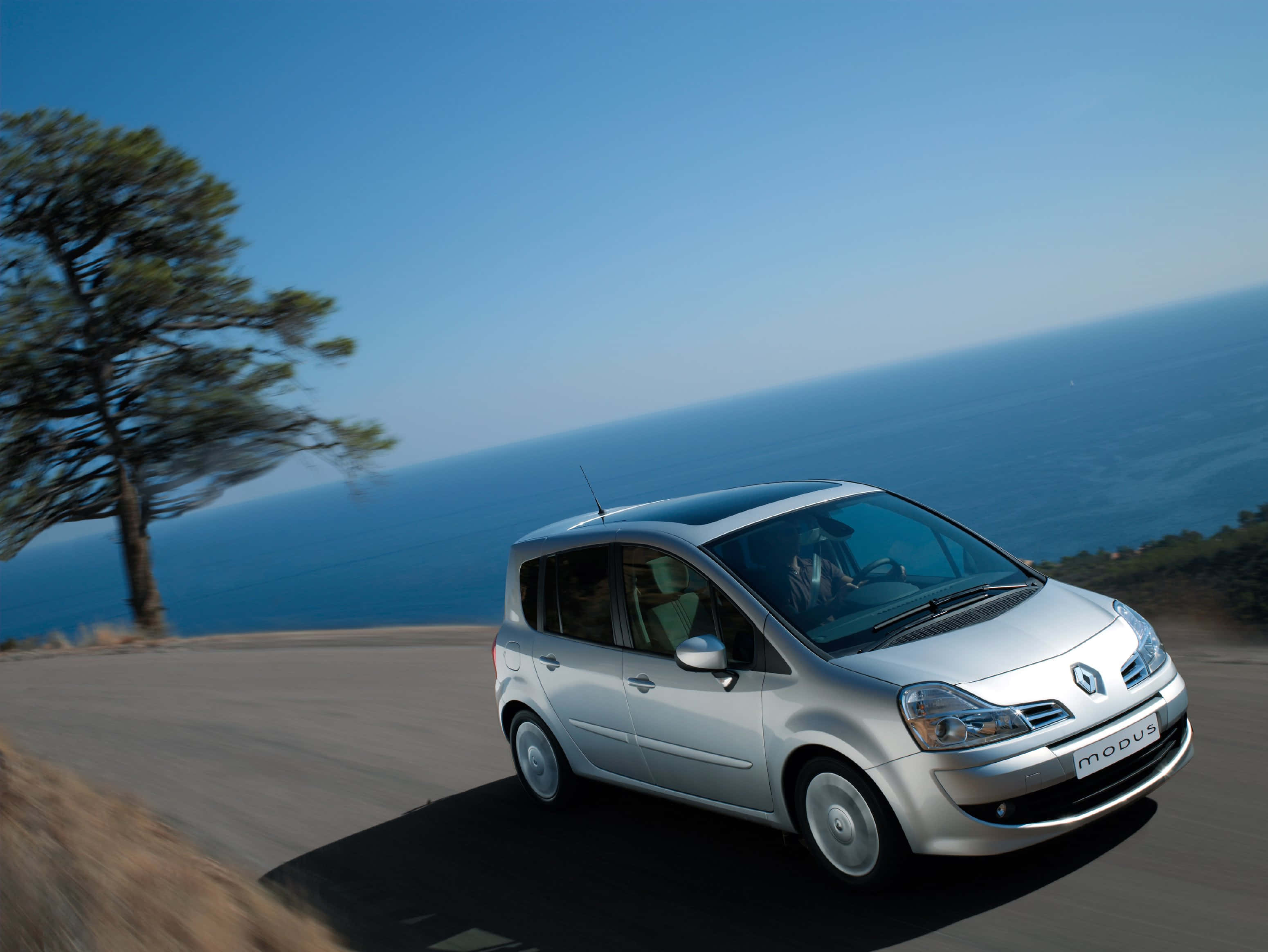 Renault Modus 桌布 壁紙 — 一輛銀色雷諾Modus沿著海岸道路行駛，背景是海洋和天空。