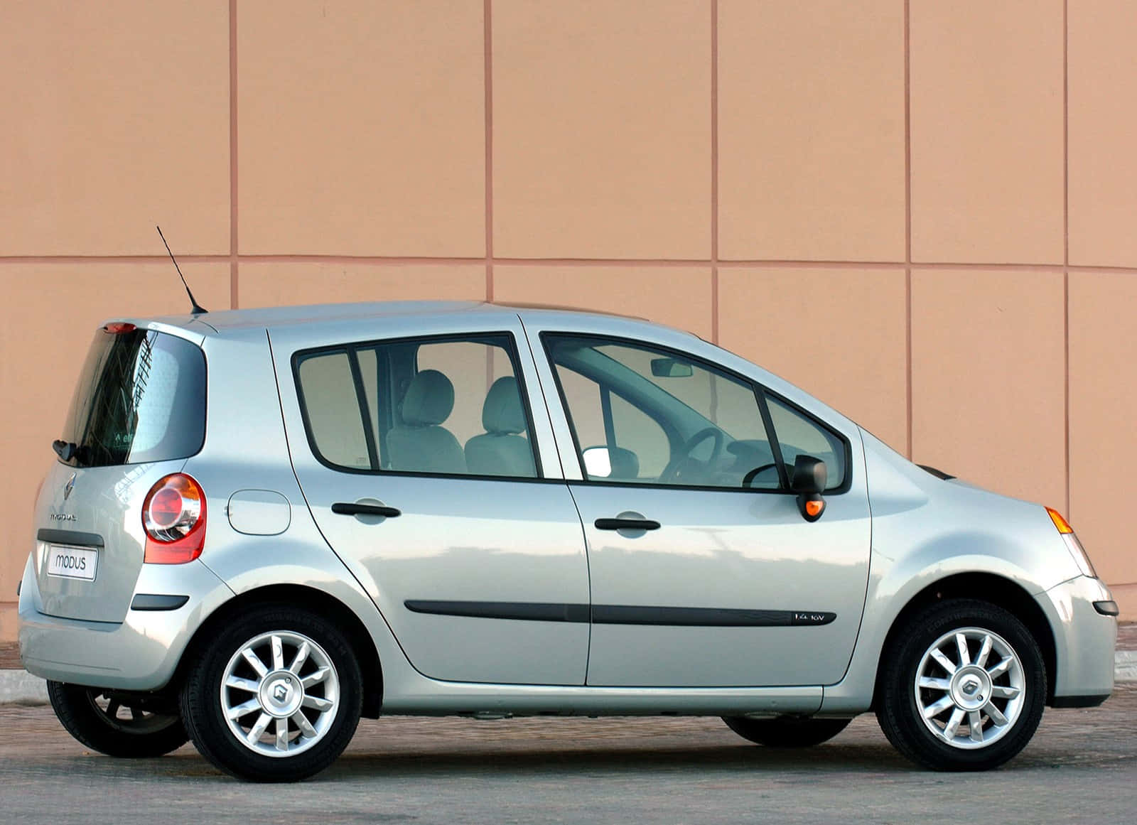 Renault Modus 桌布 壁紙 — 一輛銀色雷諾Modus緊湊型汽車在明亮的日光下停放在米色瓷磚牆前。