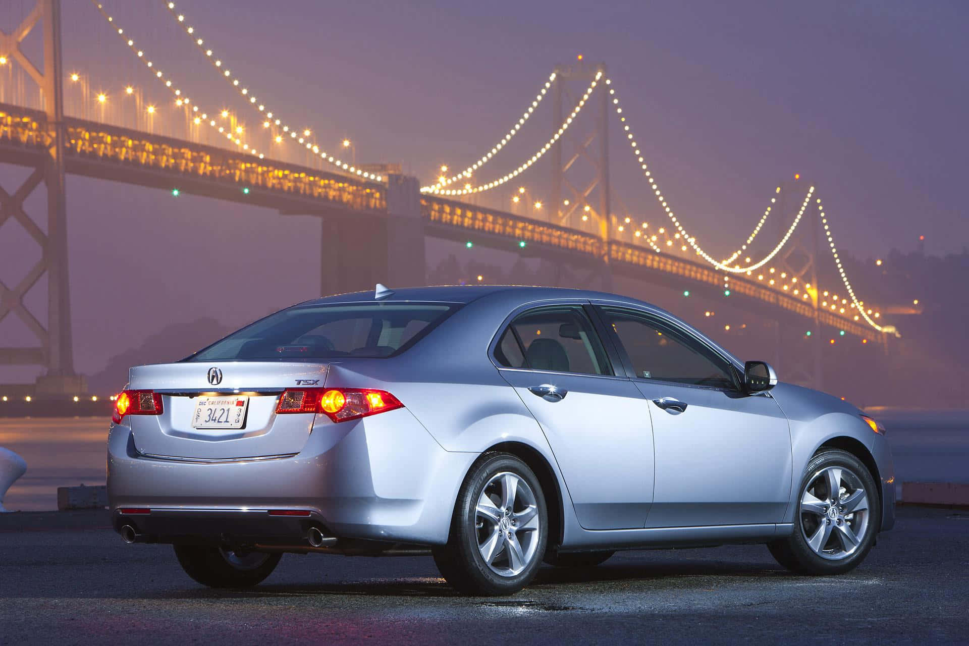 Acura Tsx 桌布 壁紙 — 一輛銀色轎車在黃昏時停泊，背景有霧氣中發光的吊橋。
