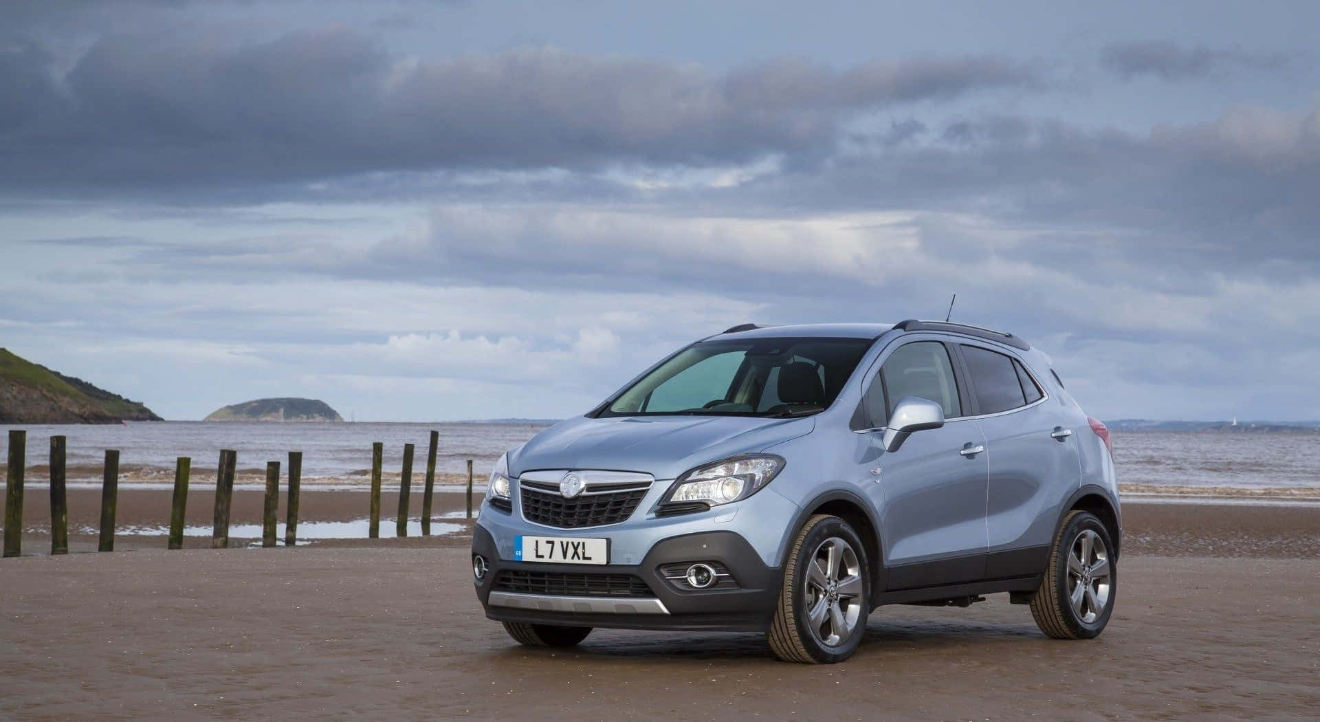 Opel Mokka 桌布 壁紙 — 一輛銀色SUV停泊在濕漉漉的海灘上，背景是陰天和遠處的海岬。