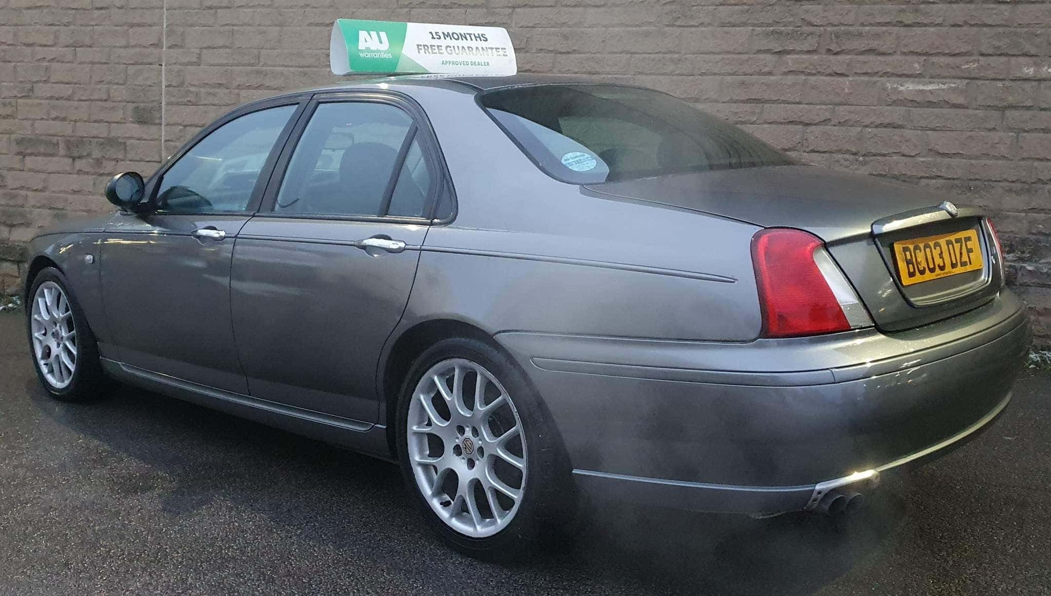 Mg Zt 桌布 壁紙 — 一輛帶有AU品牌和15個月保修標誌的銀色出租車停在磚牆旁，排放著廢氣煙霧。