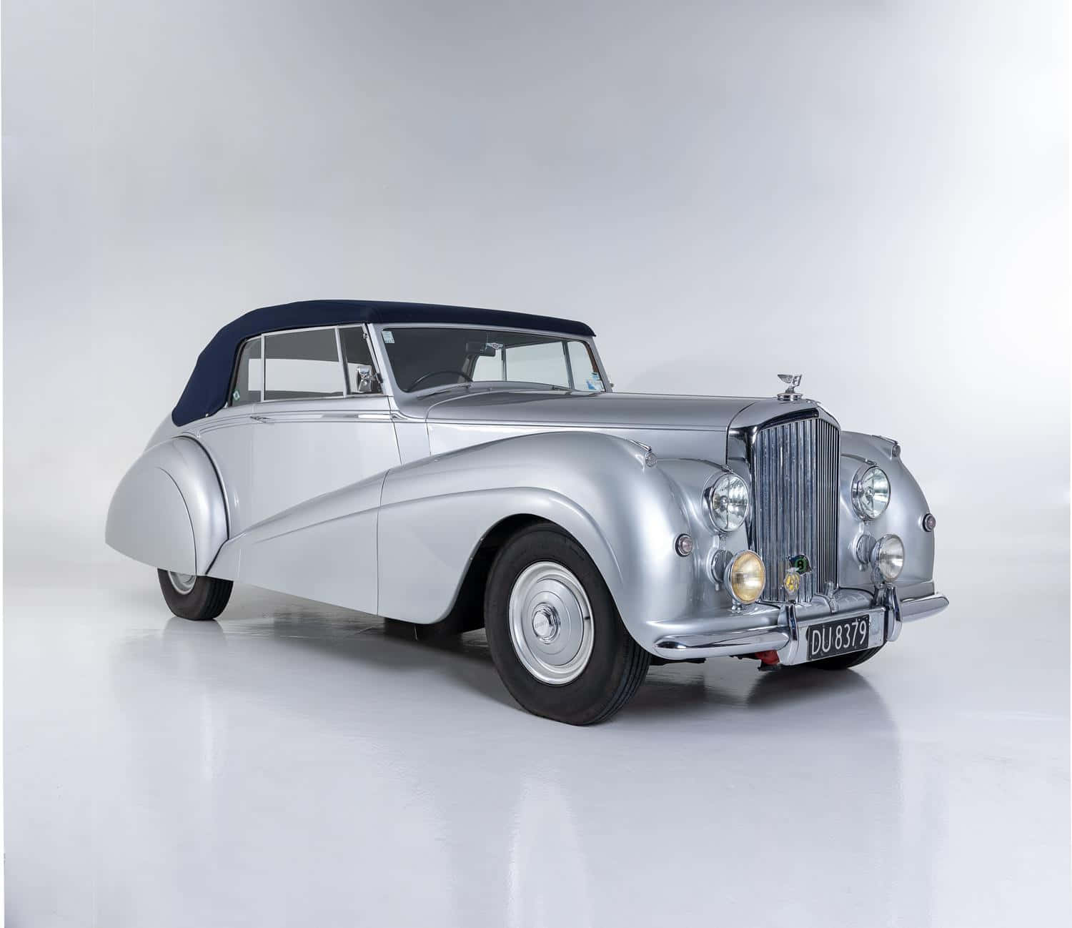Bentley Mark Vi 桌布 壁紙 — 一架時尚的銀色復古開篷車，配海軍藍軟頂，在簡約的白色工作室背景前蓄勢待發。