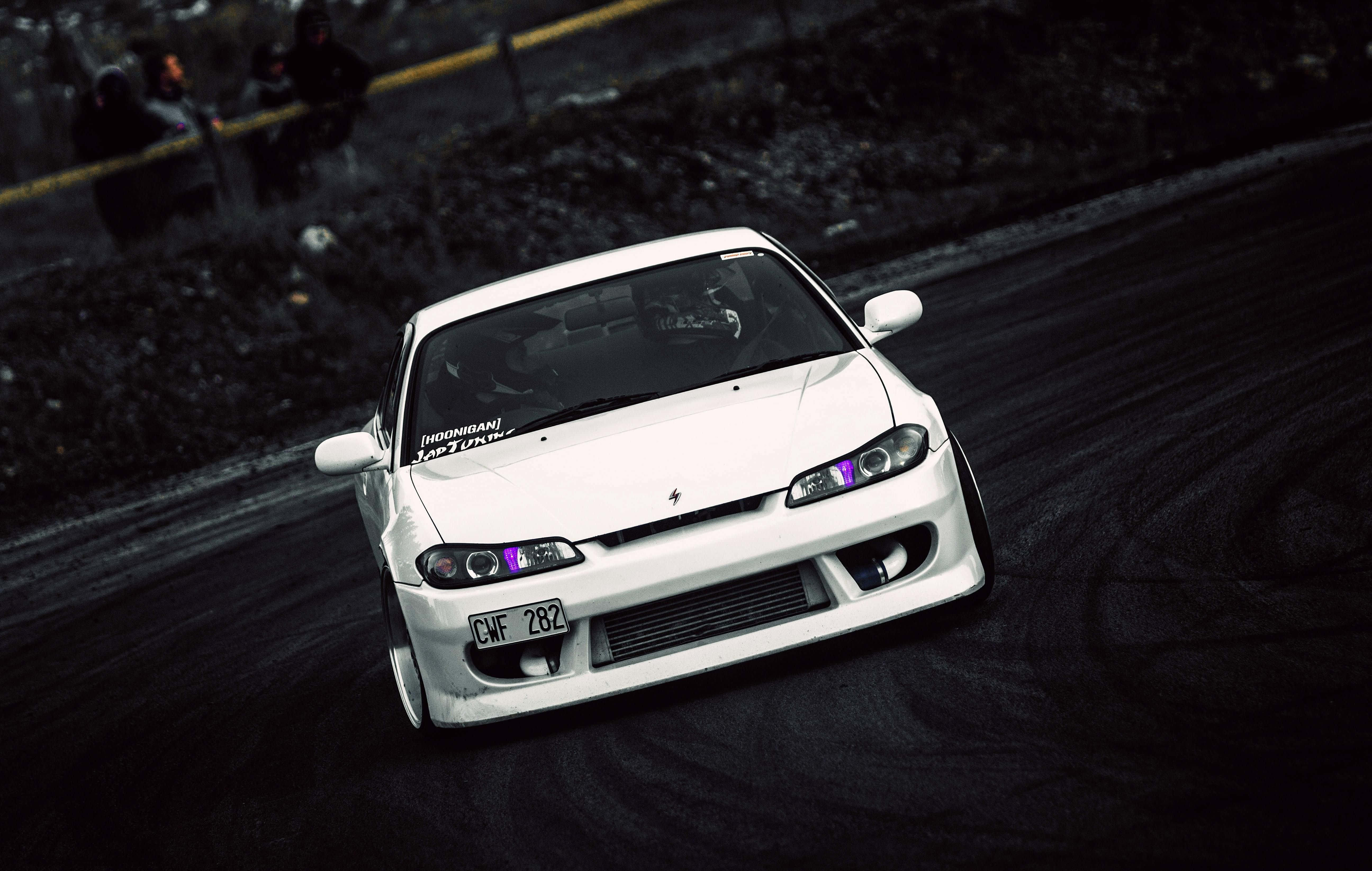 日產Silvia S15珍珠白 壁紙 — 一輛白色飄移車配紫色頭燈，在漆黑的瀝青賽道上側滑，背景有觀眾。