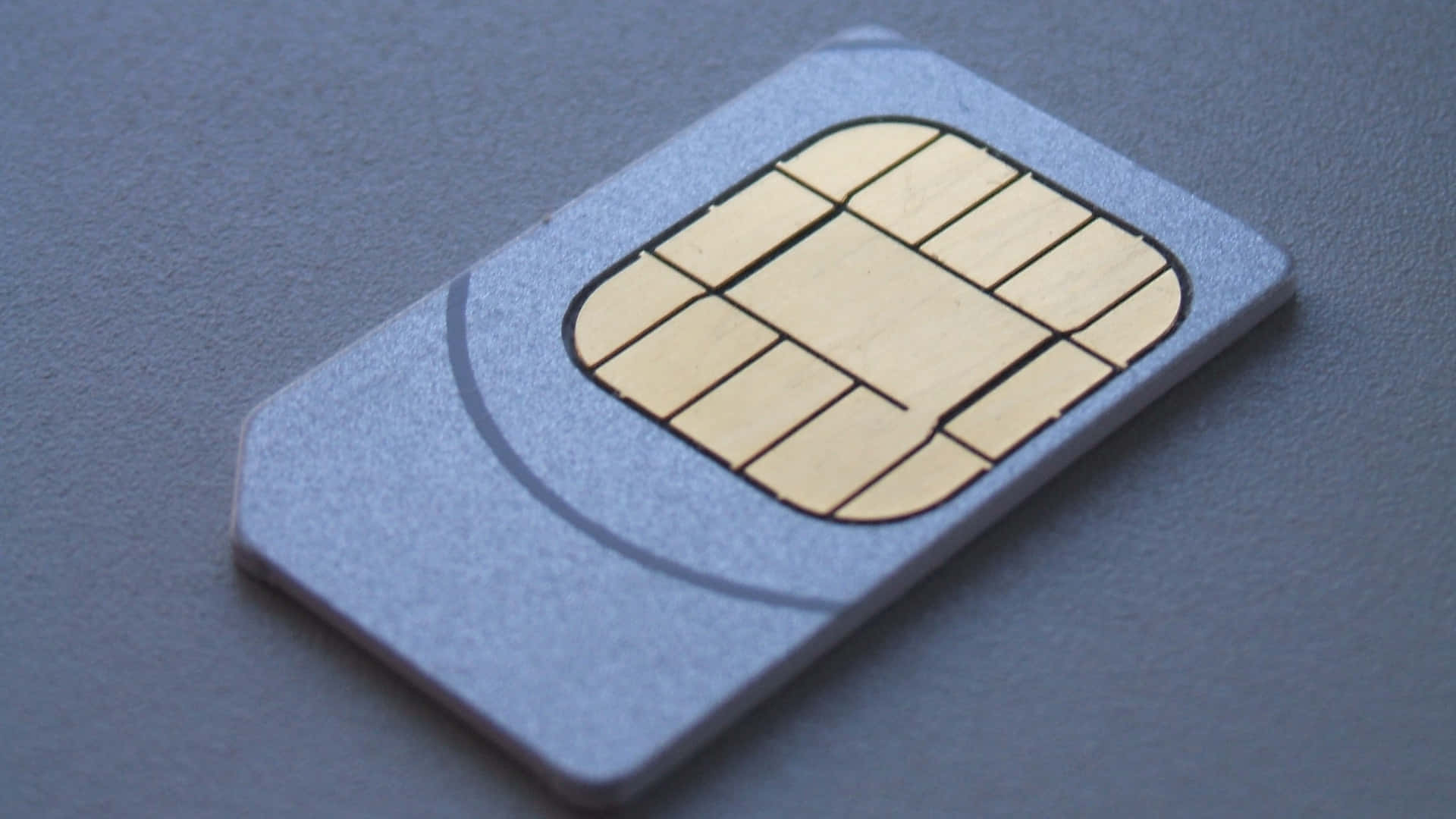 銀色SIM卡帶金色接觸點，置於紋理灰色表面上。