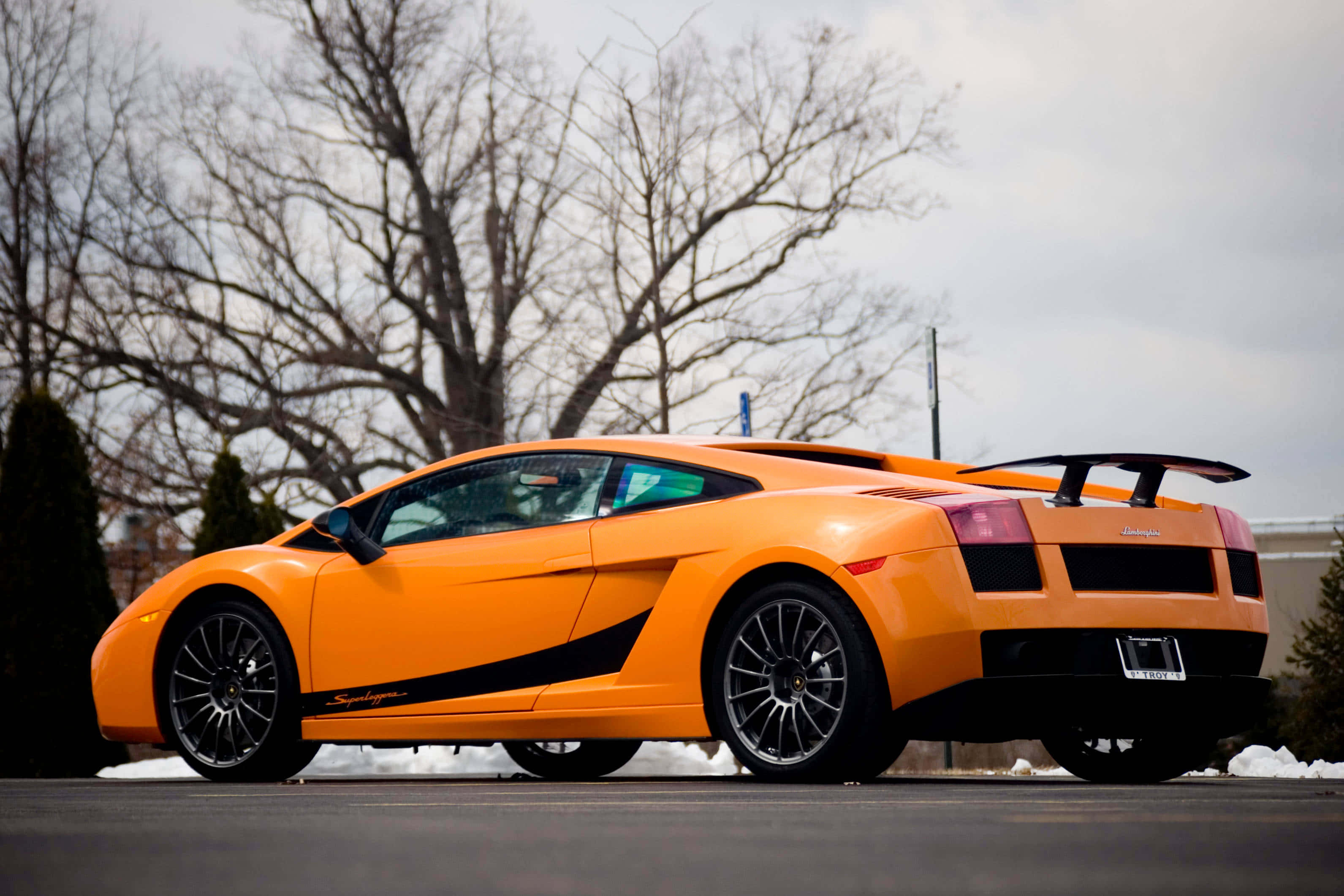 Lamborghini Gallardo 桌布 壁紙 — 一輛鮮橙色的林寶堅尼 Gallardo Superleggera 停泊在積雪的瀝青停車場，背景有光禿禿的樹木。