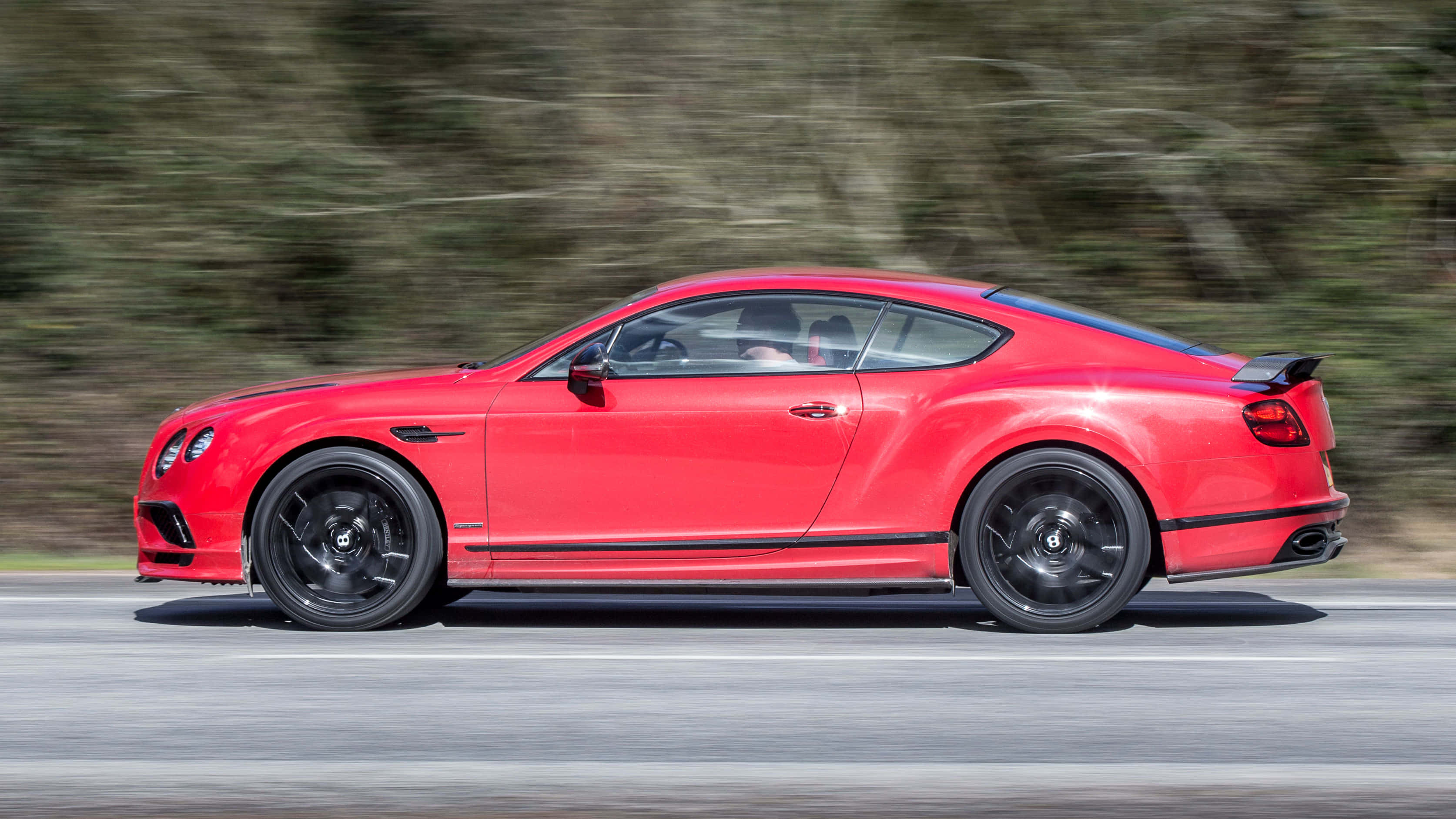 Bentley Continental Supersports 桌布 壁紙 — 一輛鮮紅色的賓利 Continental GT 在道路上疾馳，背景是模糊的綠意。