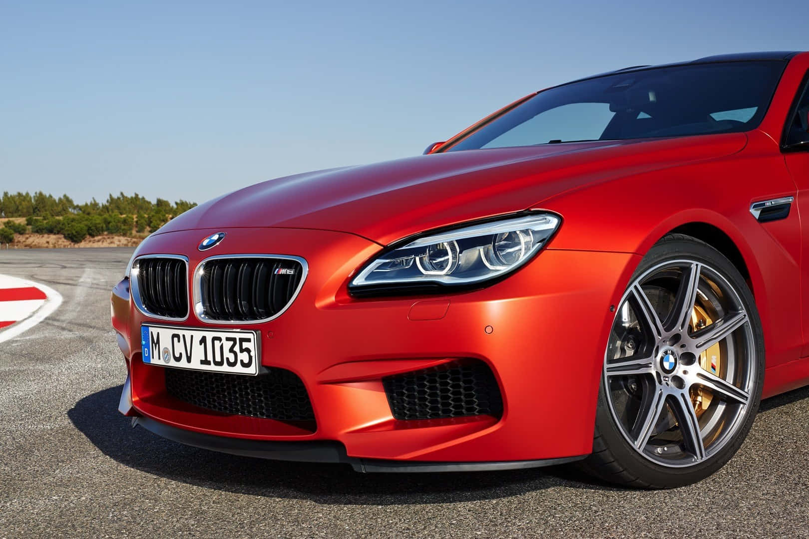 Bmw M6 桌布 壁紙 — 一輛鮮紅色的BMW M6跑車在晴朗藍天和遠處樹木的賽道上，在明亮的陽光下閃閃發光。