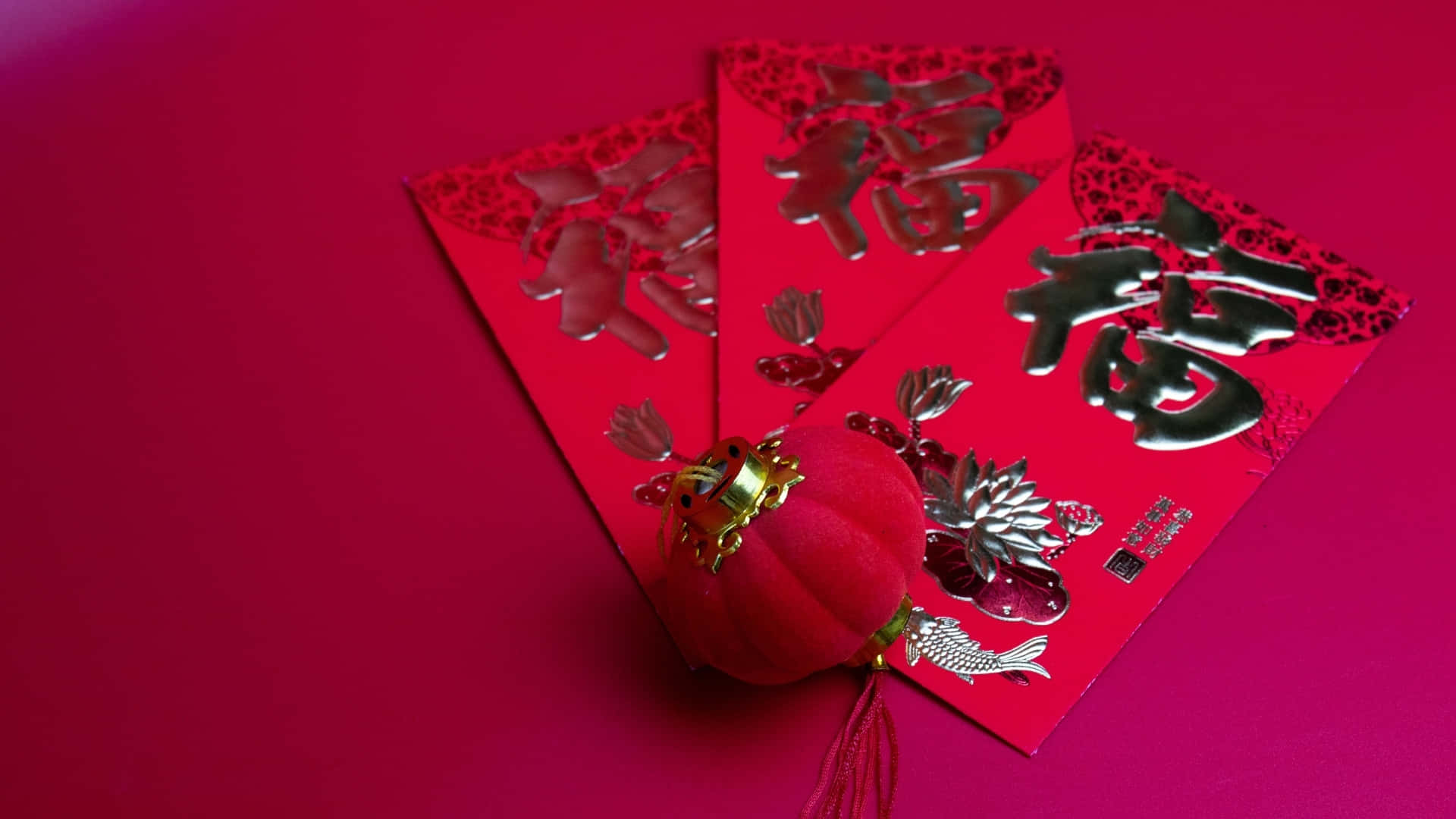  壁紙 — 鮮紅色的利是封帶有銀色中文字，以及一個毛絨紅燈籠，放在相配的紅色表面上。