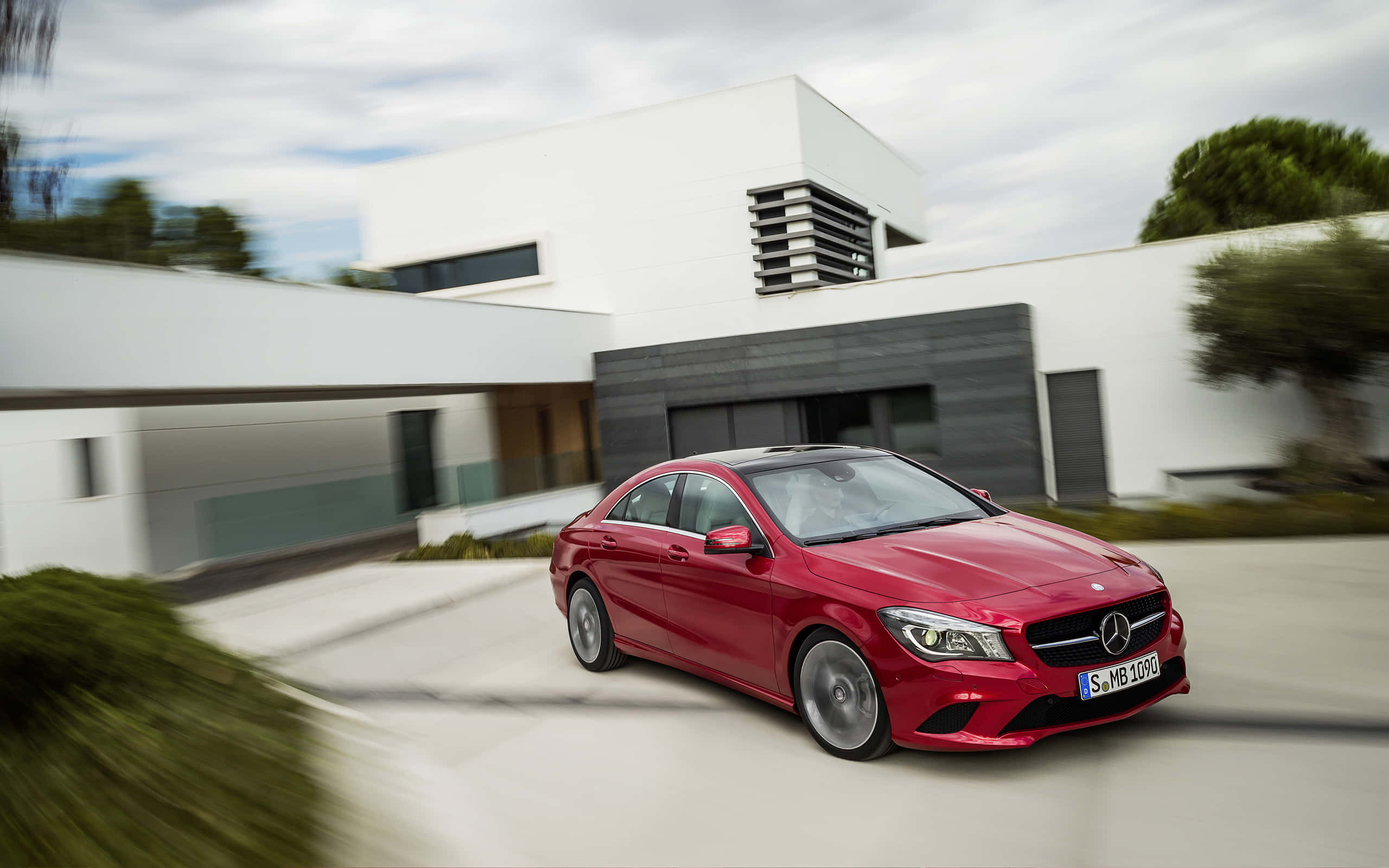 Mercedes Benz Cla-class 桌布 壁紙 — 一輛鮮紅色的 Mercedes-Benz CLA 房車以動態模糊效果駛過一棟現代白色房屋。
