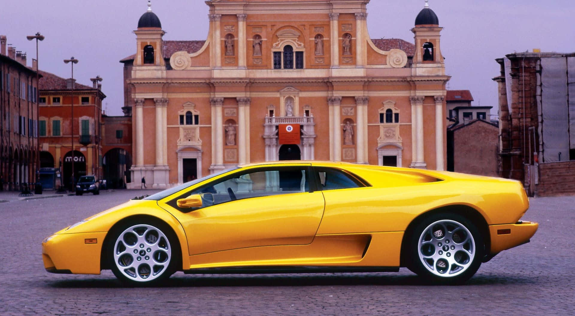 Lamborghini Diablo 桌布 壁紙 — 一輛鮮黃色的林寶堅尼 Diablo 跑車在黃昏時停在一座宏偉的歐洲教堂前。