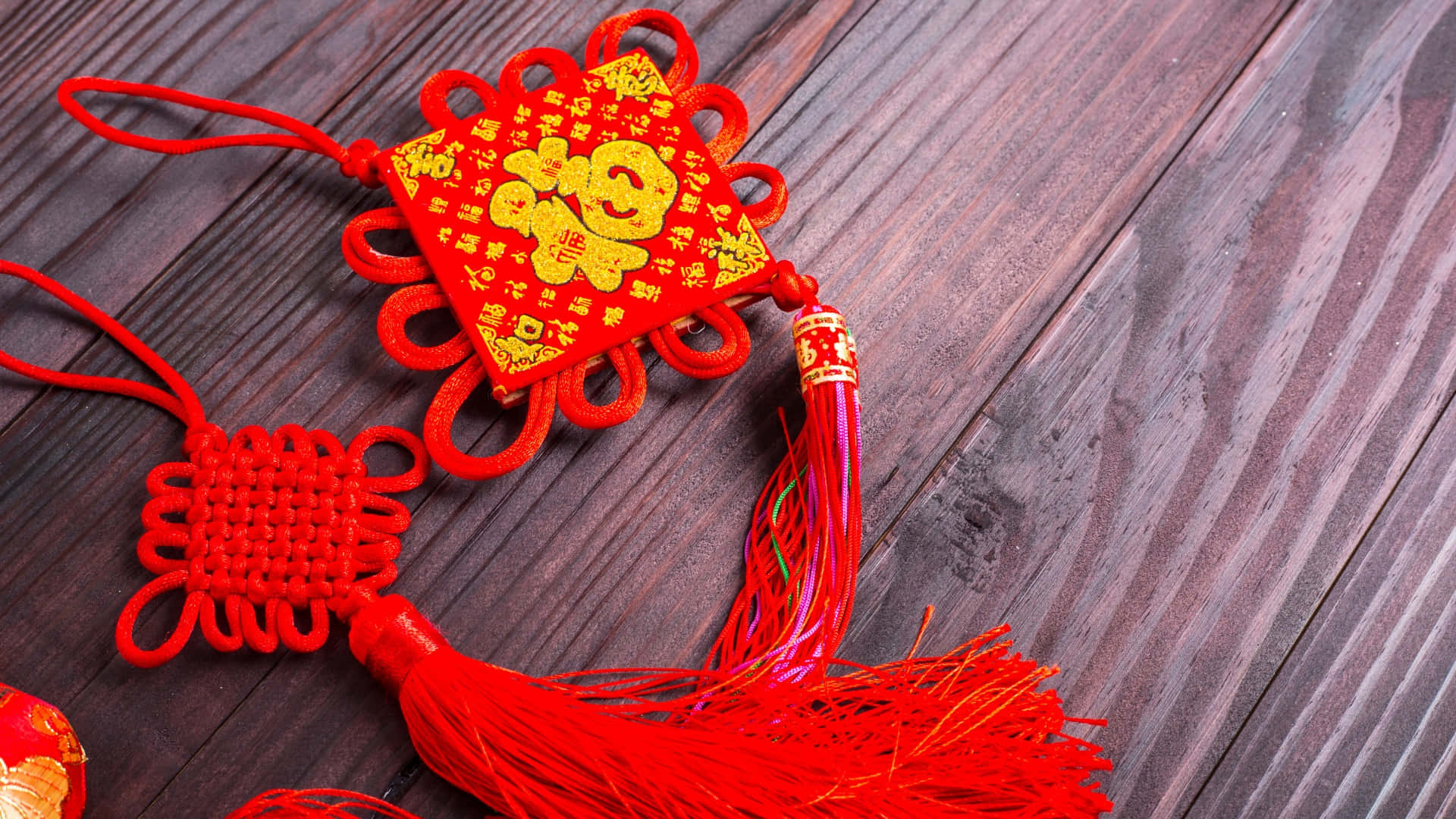  壁紙 — 鮮豔的紅色中國結裝飾品，帶有金色的「福」字，放置在深色木板上。