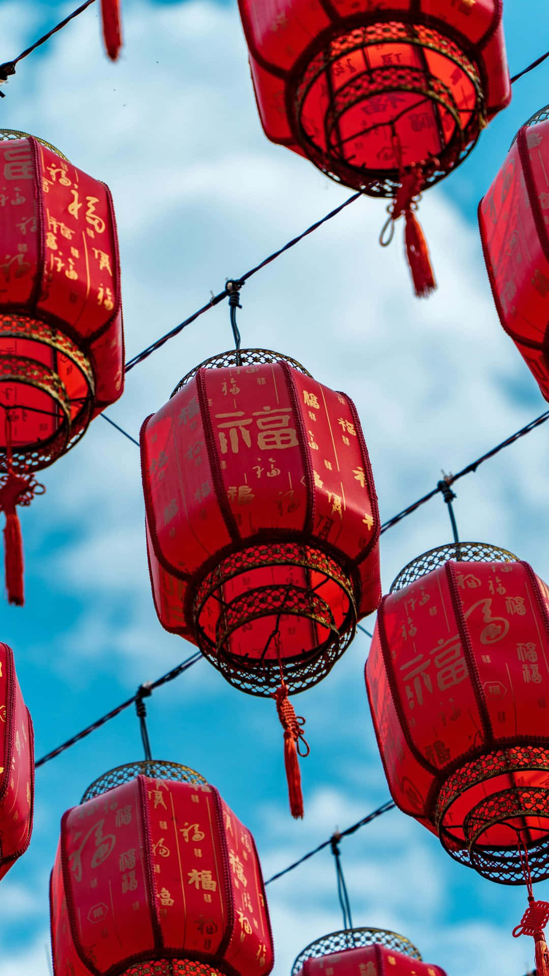  壁紙 — 鮮豔的紅色中國燈籠掛著金色字體，襯托著帶有薄雲的明亮藍天。